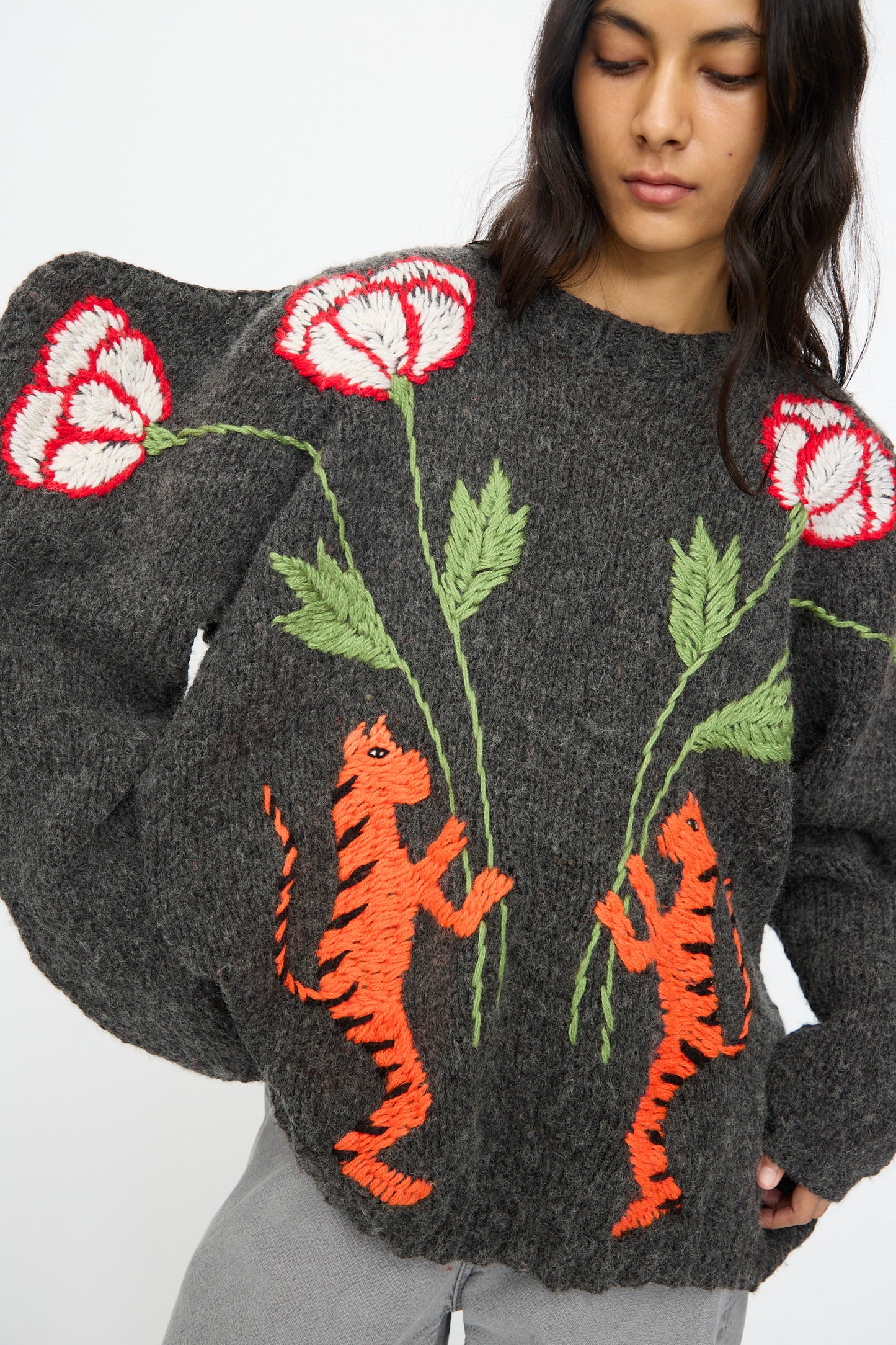 A person wears the Sofio Gongli Sweater in Charcoal with Tigers and Flowers, a mohair wool blend with large puffed sleeves, adorned with hand-embroidered red and white flowers and two upright orange tigers.