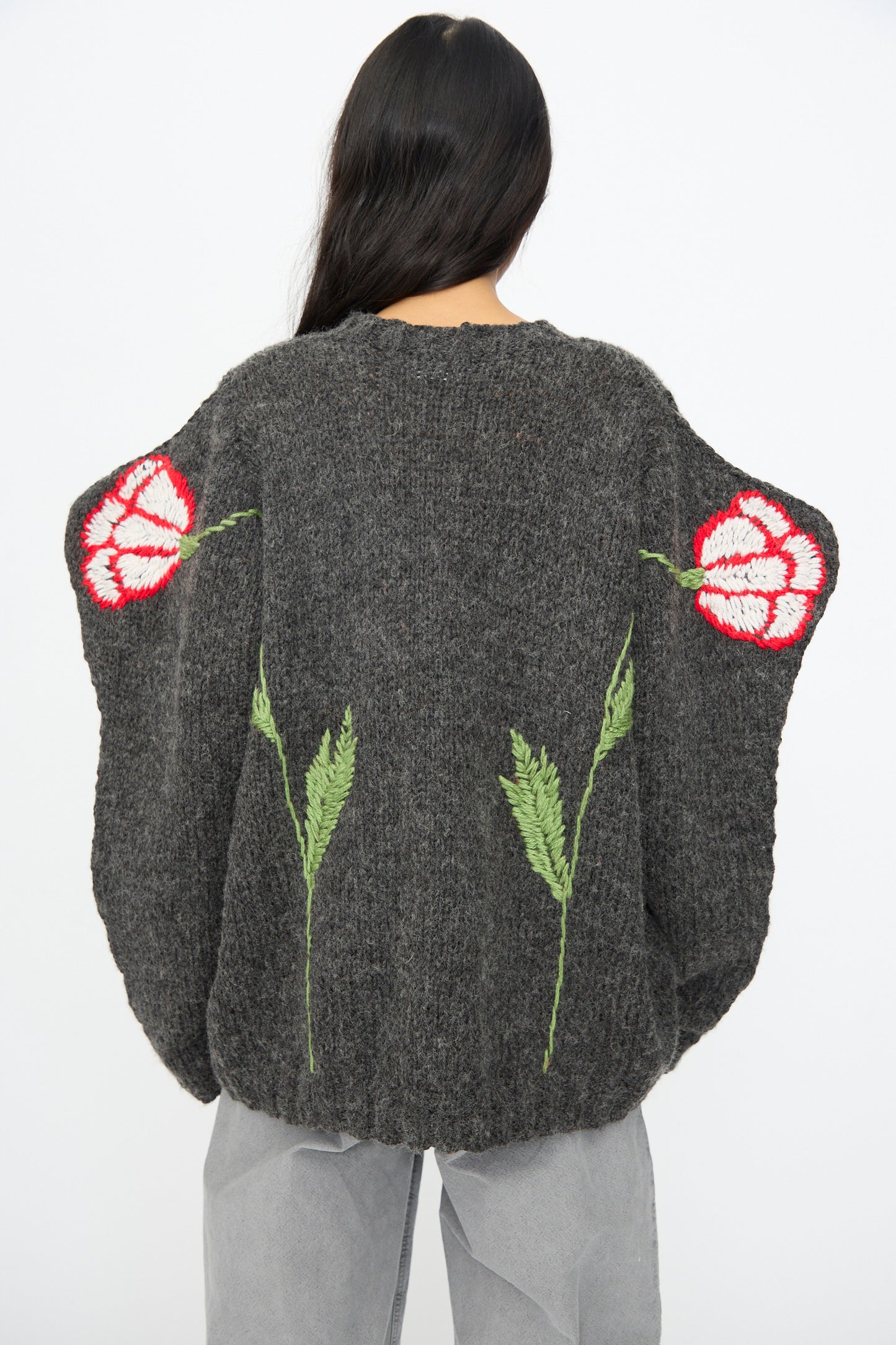 A person with long dark hair wears the Sofio Gongli Sweater in Charcoal with Tigers and Flowers, a loose-fitting hand-knit piece, styled with light gray pants.