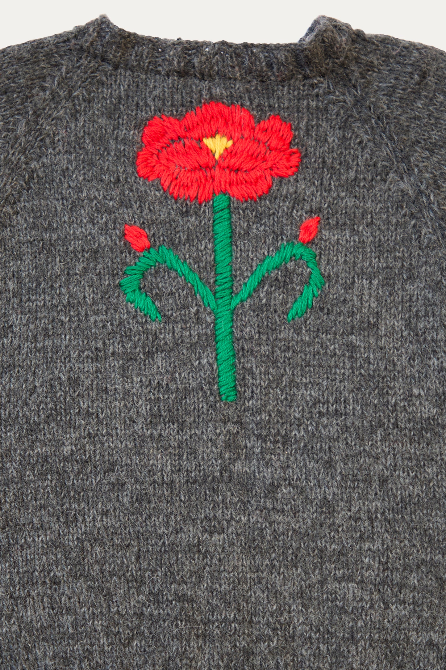 A close up of a harcoal sweater by Sofio Gongli featuring a vibrant embroidered flower design in red and pink.