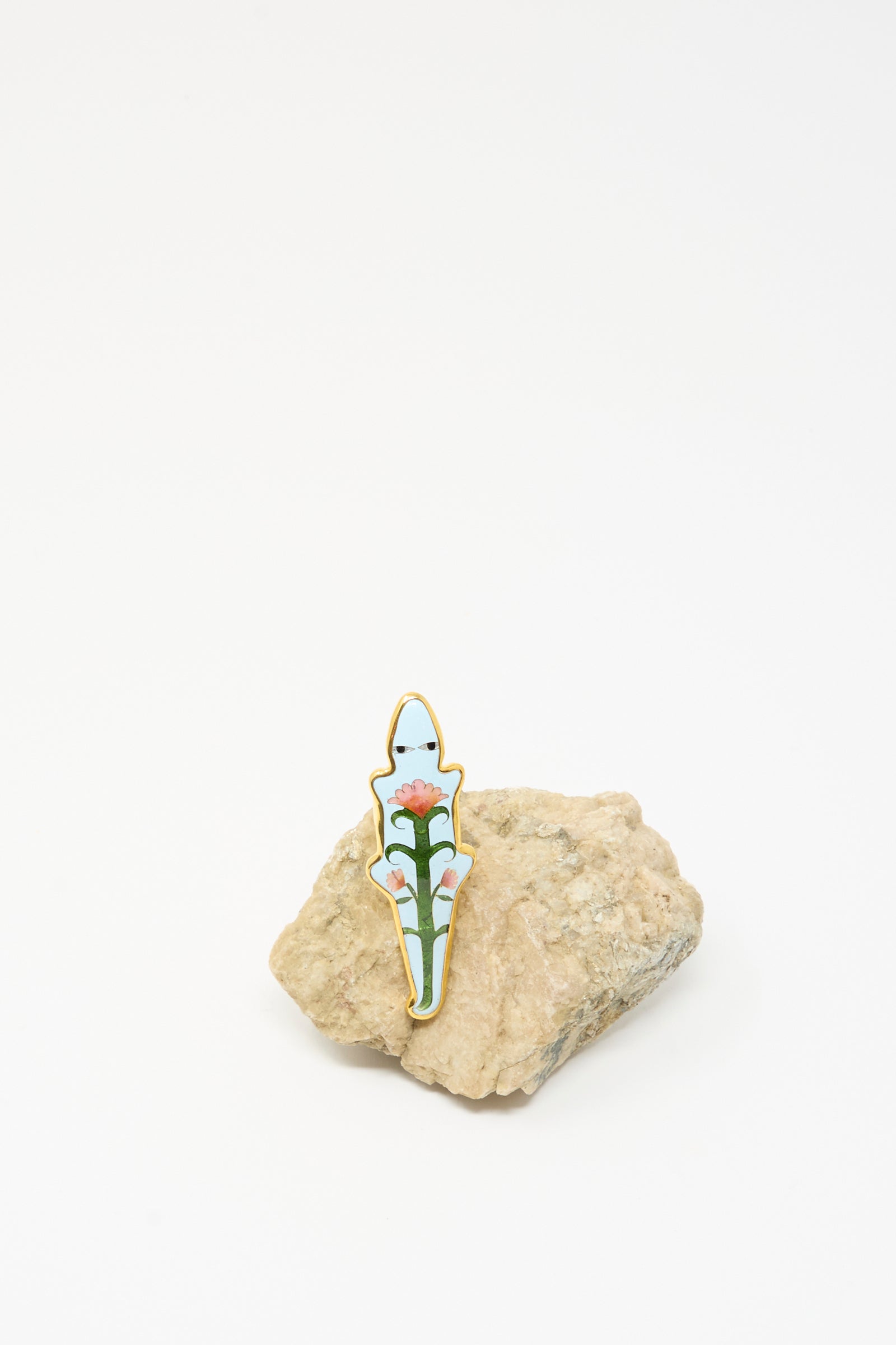 The Alligator Ring in Blue by Sofio Gongli is shown upright on a rough beige rock, its blue enamel and charming details reminiscent of cloisonné art, all set against a plain white background.