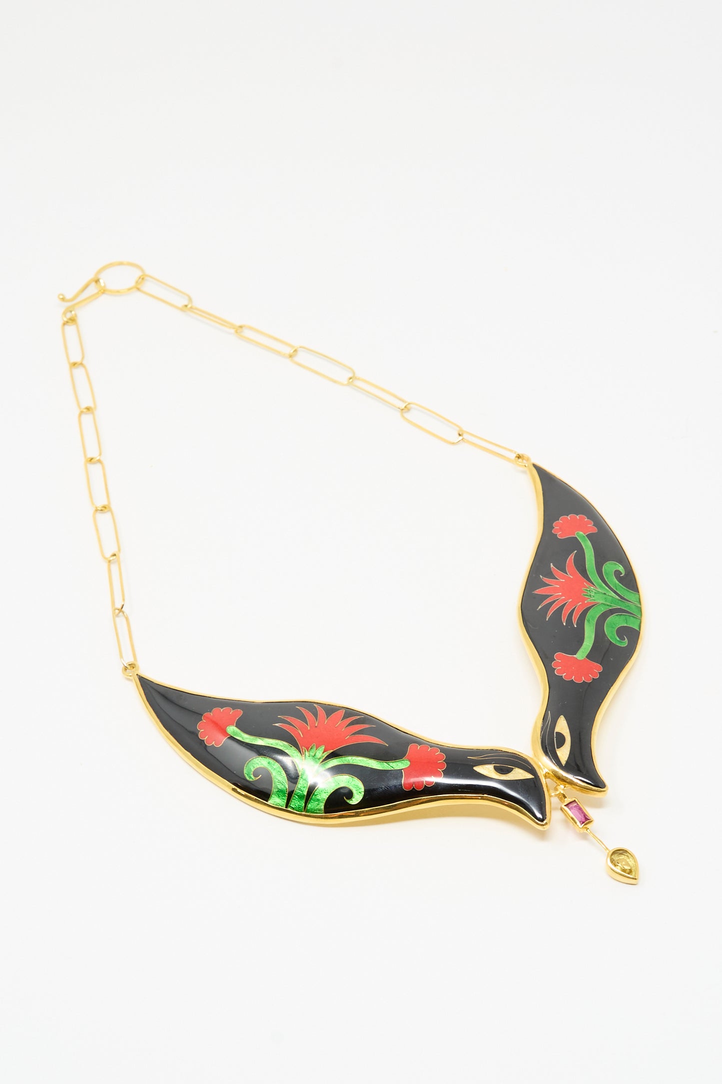 The Bird Necklace in Black and Red Flower by Sofio Gongli features 14K gold plating, two black leaf-shaped pendants with red and green floral designs, and a small dangling jewel.