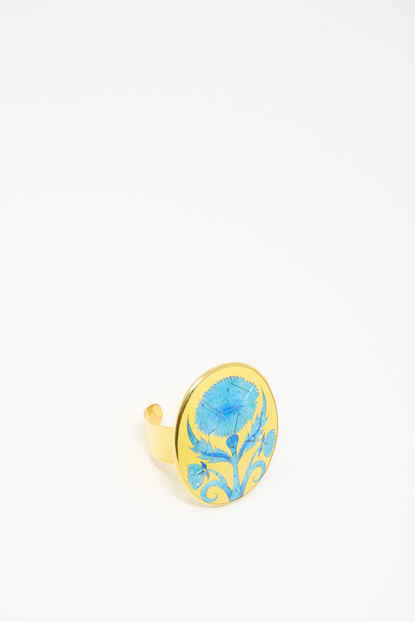 The Flower Bracelet in Blue by Sofio Gongli features a wide circular face adorned with a blue floral design inspired by Byzantine cloisonné art, displayed against a plain white background.
