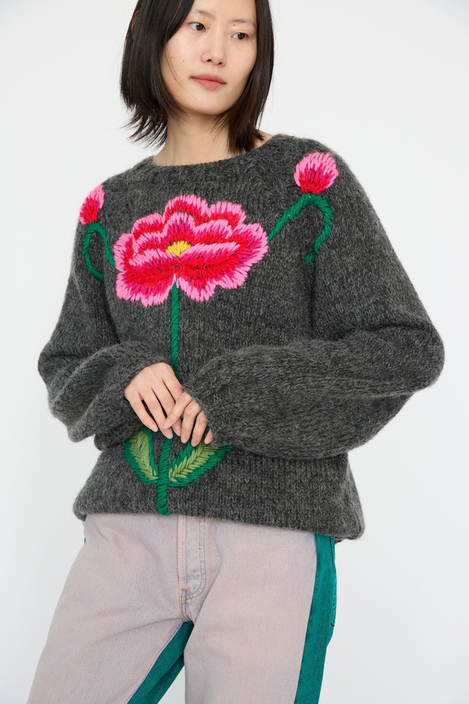 A person wearing Sofio Gongli's "Sweater with Red and Pink Flower in Charcoal" stands against a plain background.