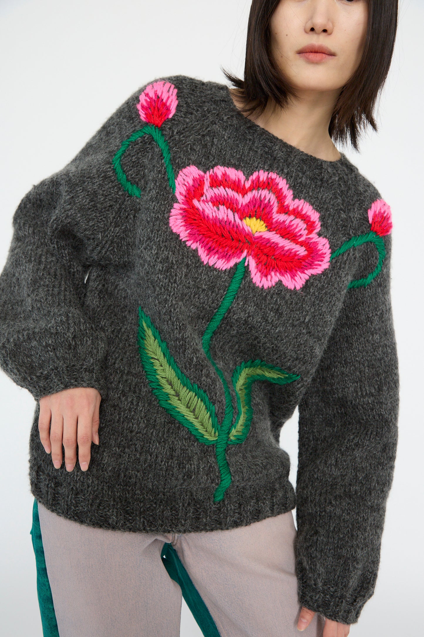 Someone models the Sofio Gongli charcoal sweater, which features a striking red and pink floral design, against a simple backdrop.