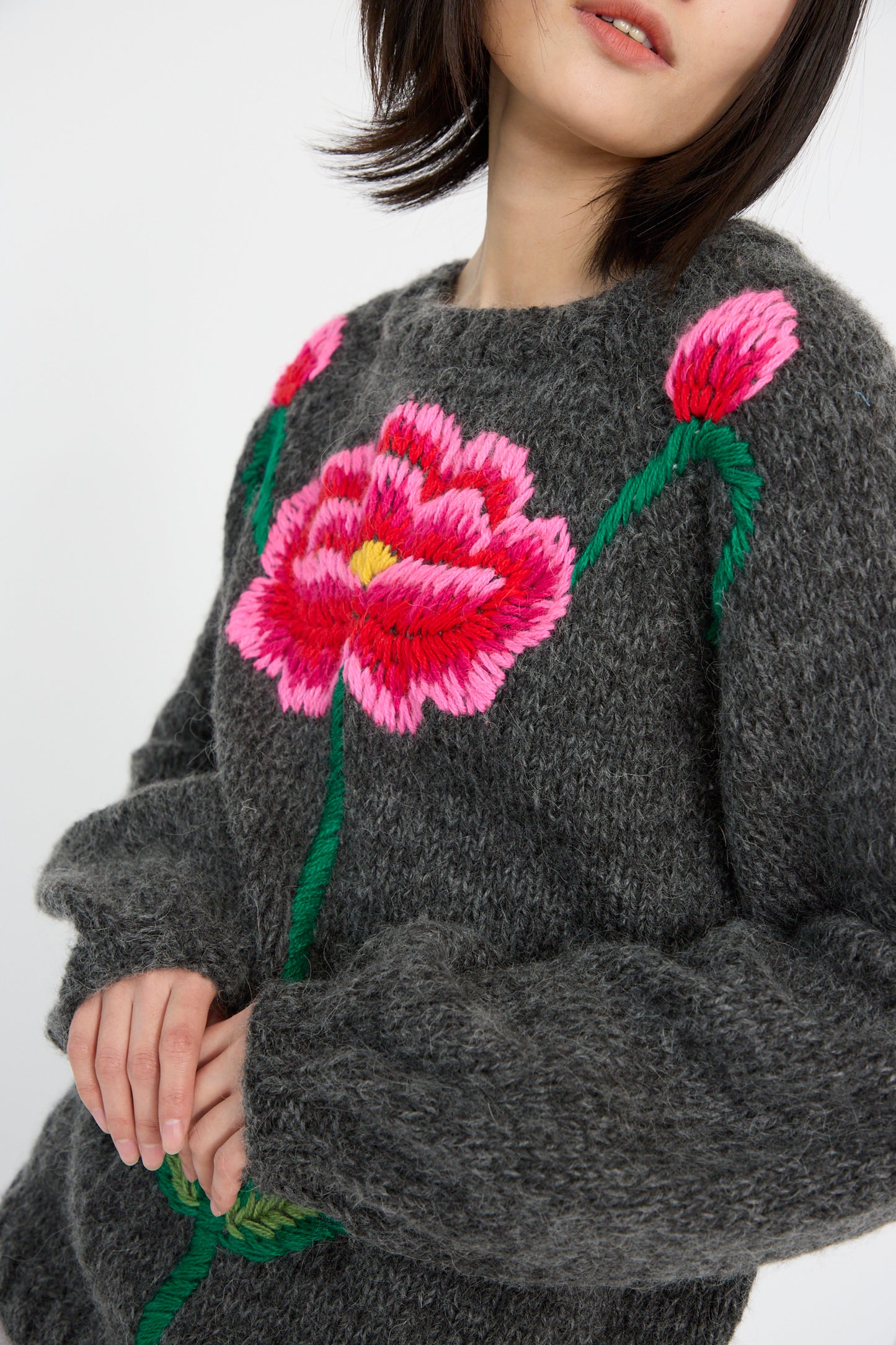 A person wearing a Sofio Gongli charcoal sweater with red and pink flowers, hand-knit from a mohair wool blend.