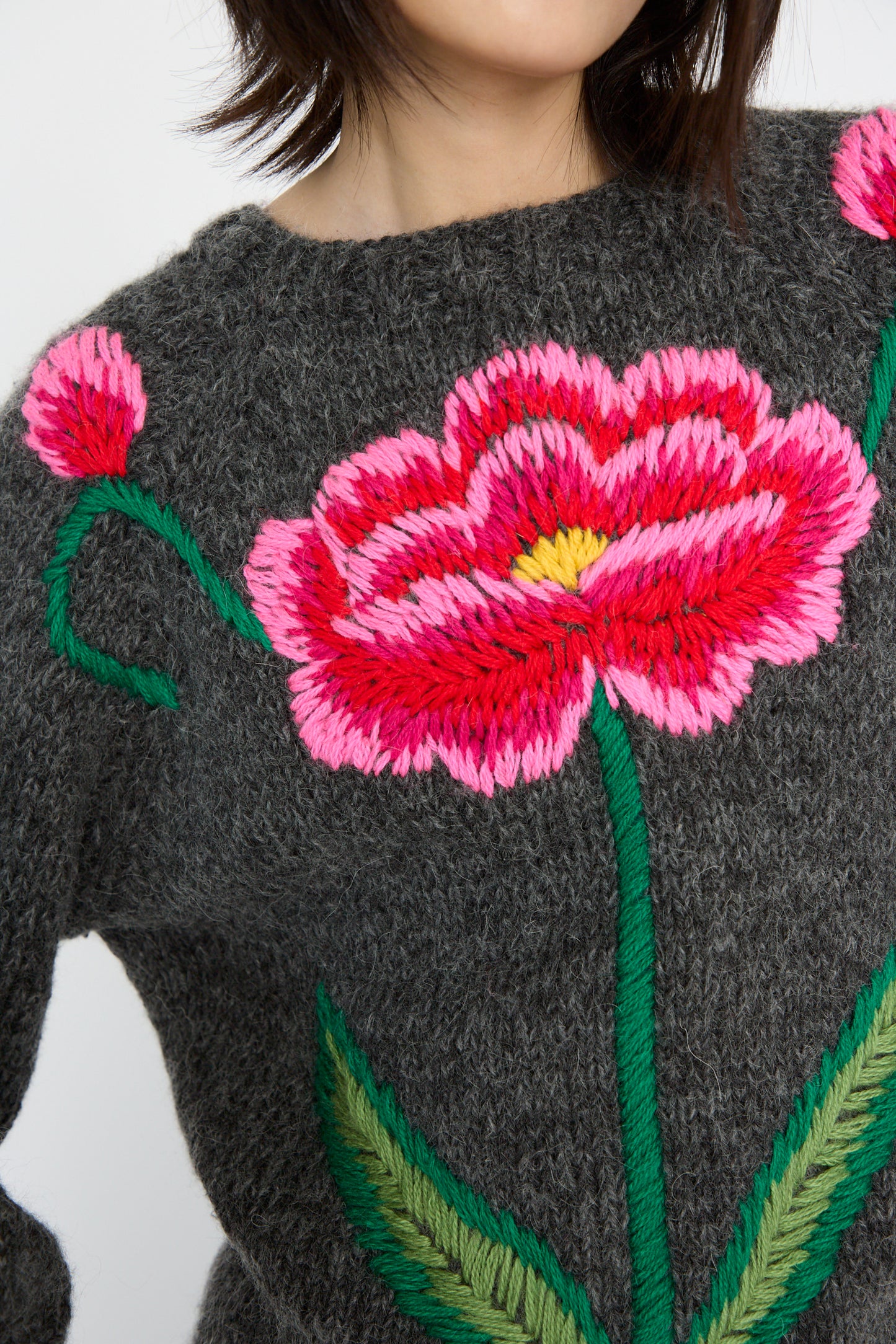 Charcoal knit sweater by Sofio Gongli featuring a hand-embroidered red and pink flower with green leaves.