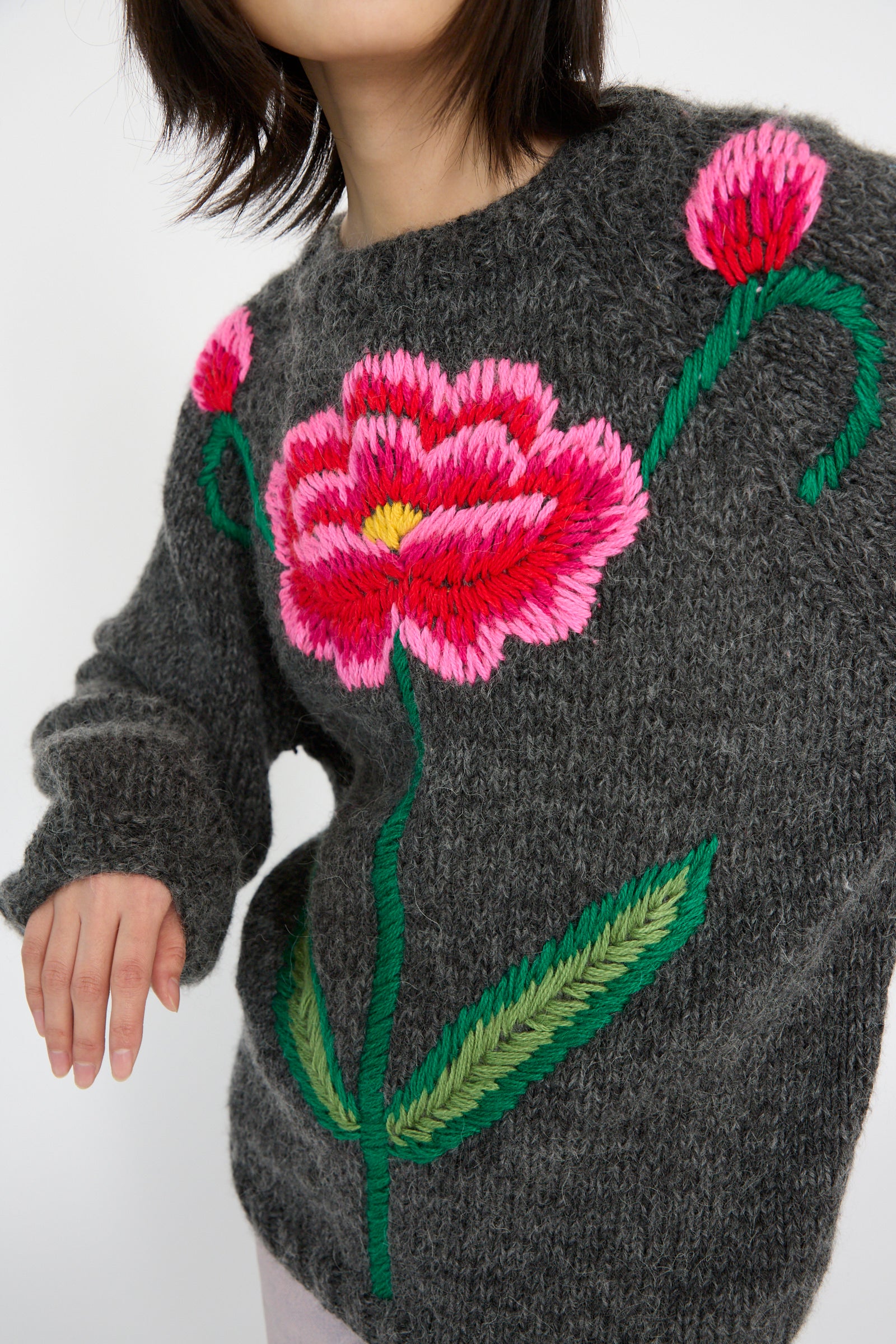 A person wearing a Sofio Gongli "Sweater with Red and Pink Flower in Charcoal" features large floral embroidery on the front against a plain background.