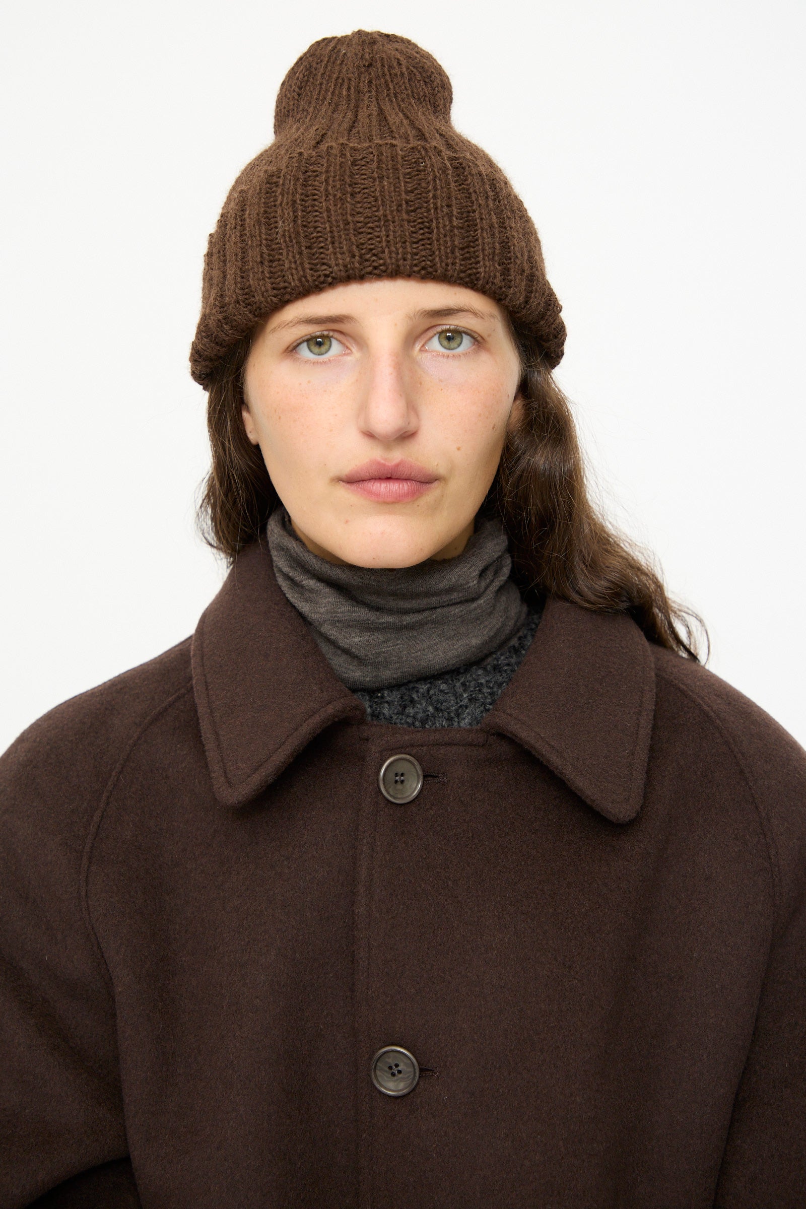 A person wears the SONO Alpaca and Wool Gyu Beanie in Terra, a brown coat, and a gray turtleneck, looking directly at the camera against a plain white background.