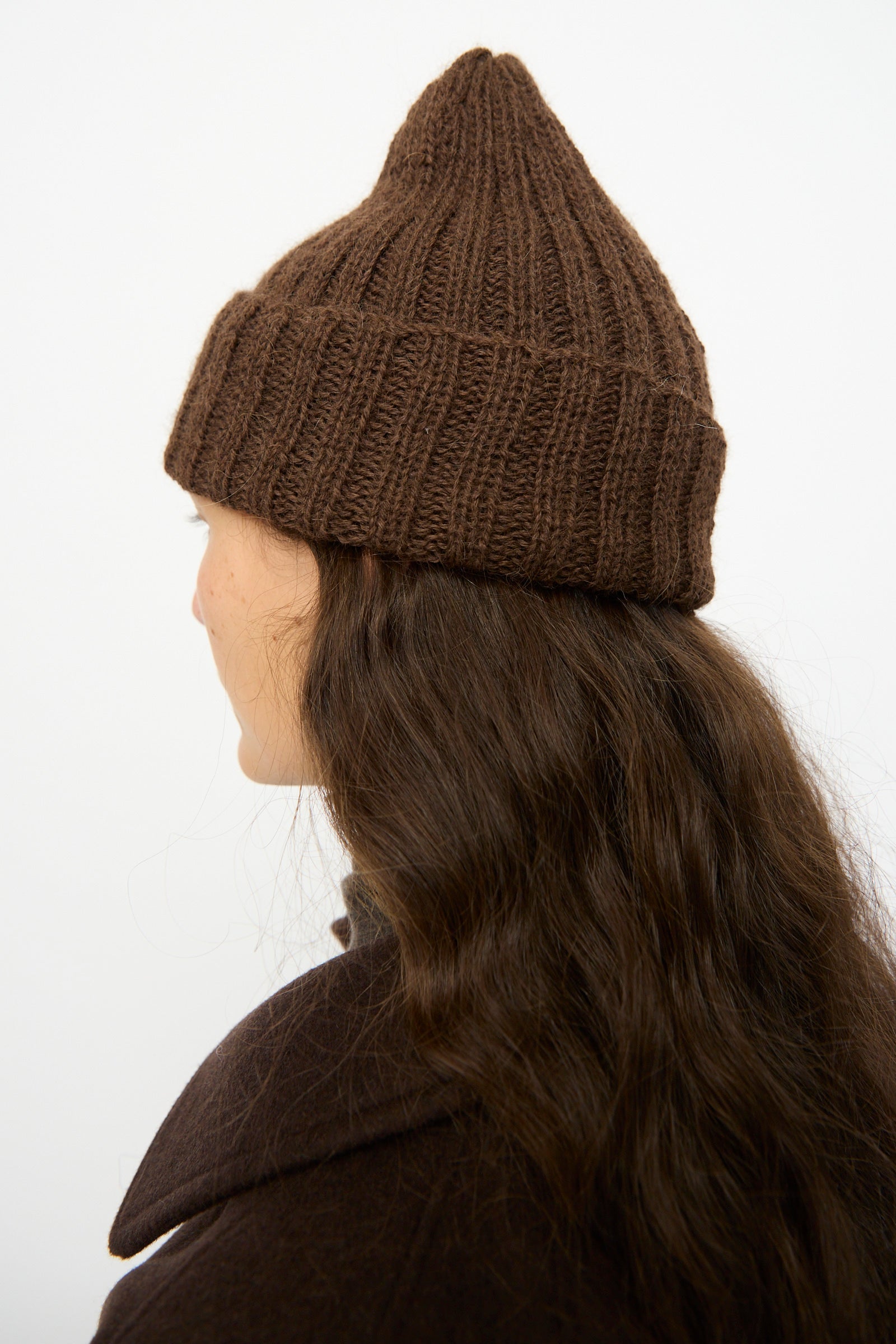 A person with long wavy brown hair, shown from behind against a plain background, is wearing the SONO Alpaca and Wool Gyu Beanie in Terra.