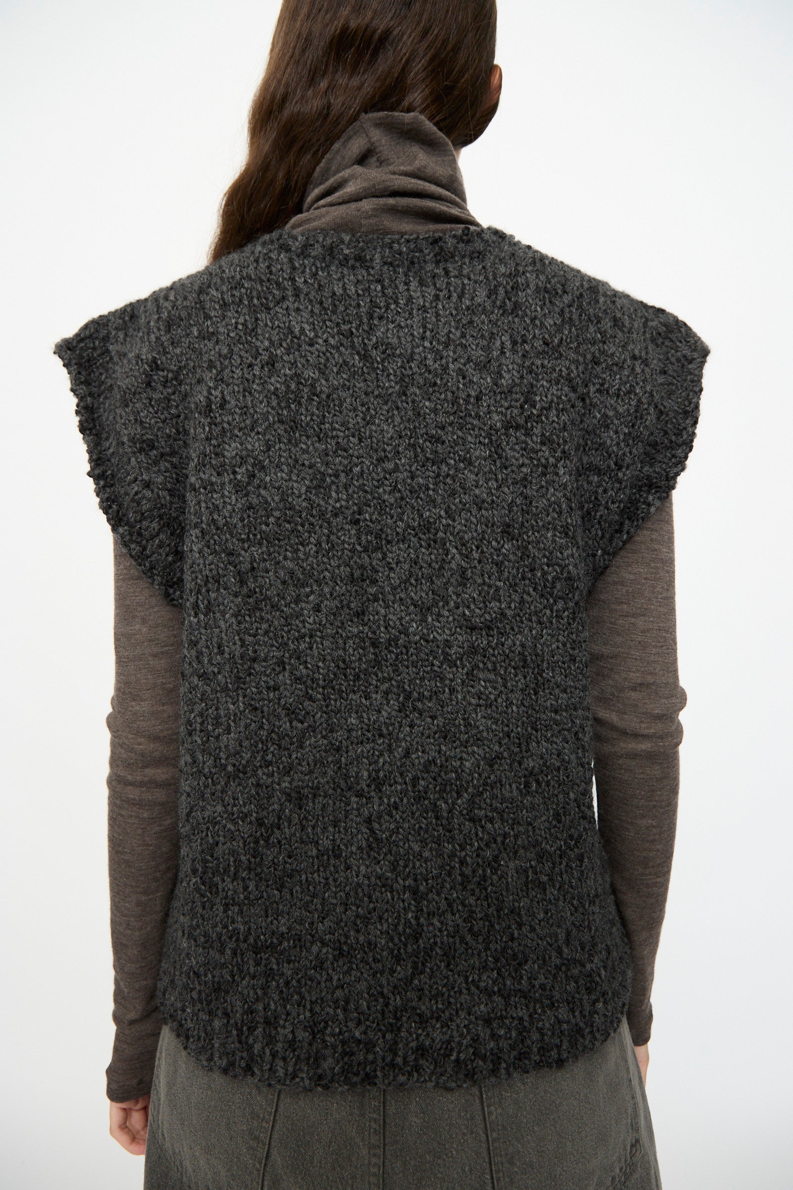Person facing away, wearing the SONO Alpaca and Wool Petras Pullunder in Charcoal—made in the UK—over a long-sleeve, high-neck brown top and dark pants.