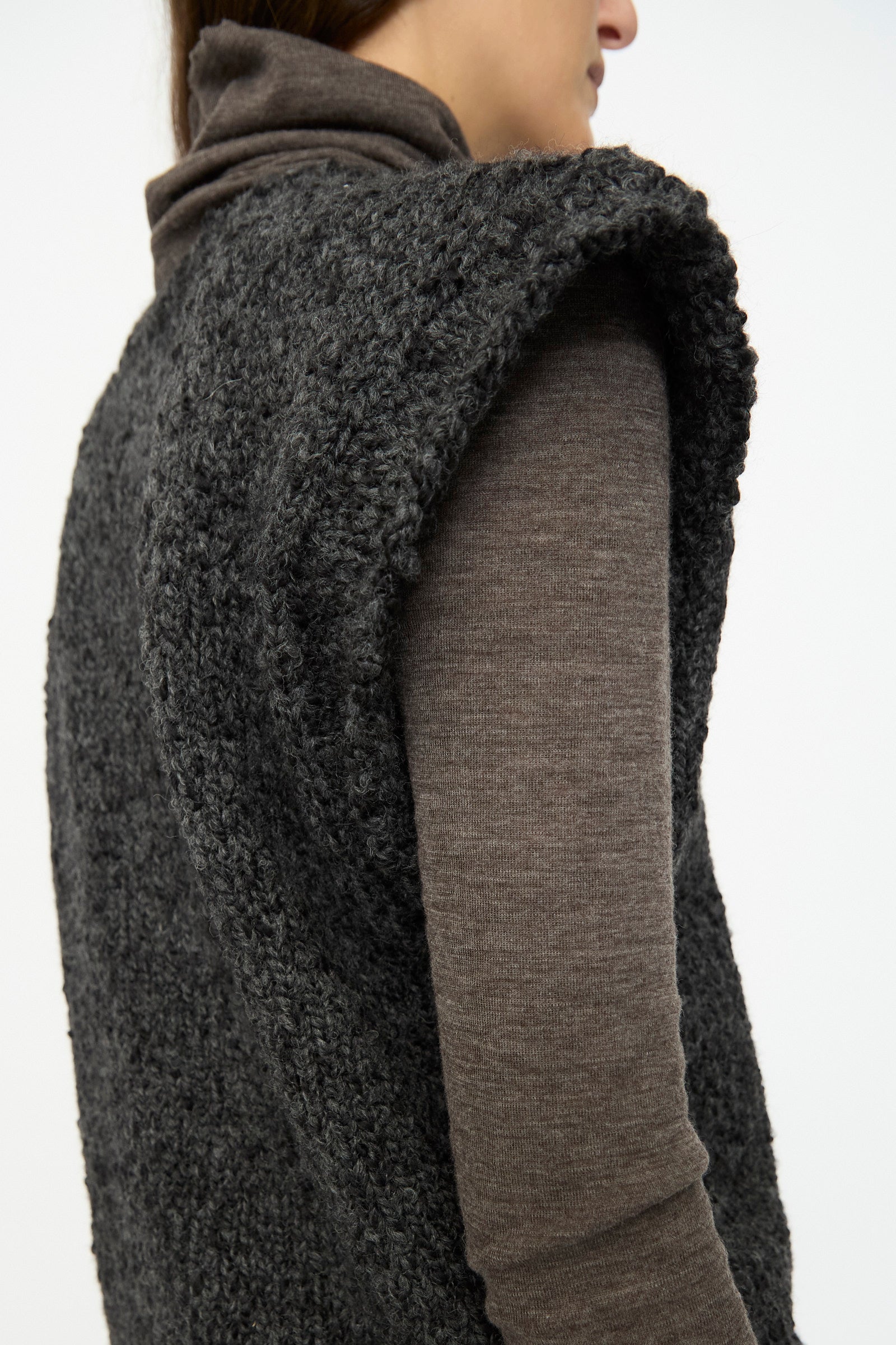A person wears the SONO Alpaca and Wool Petras Pullunder in Charcoal—a chunky, textured vest—over a brown turtleneck, shown from the side against a plain background.