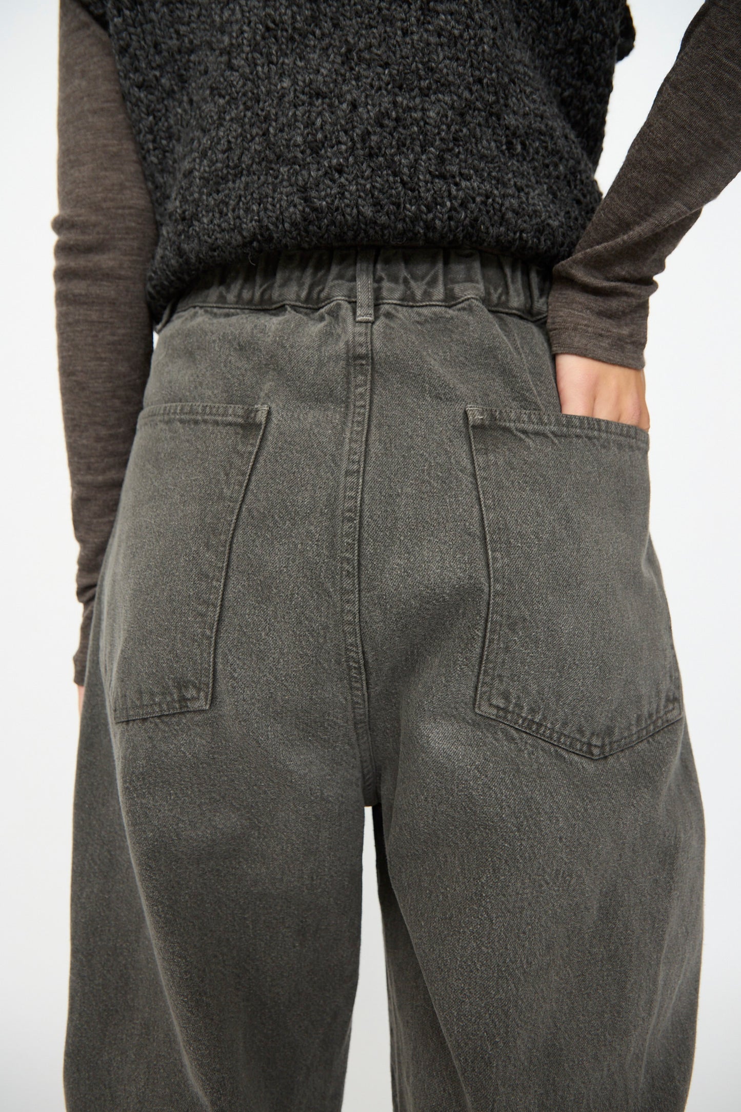 Someone is wearing SONO’s Cotton Jah Jeans in Off Black—high-waisted, loose-fit organic denim with back pockets—paired with a textured black top, right hand resting on their hip.