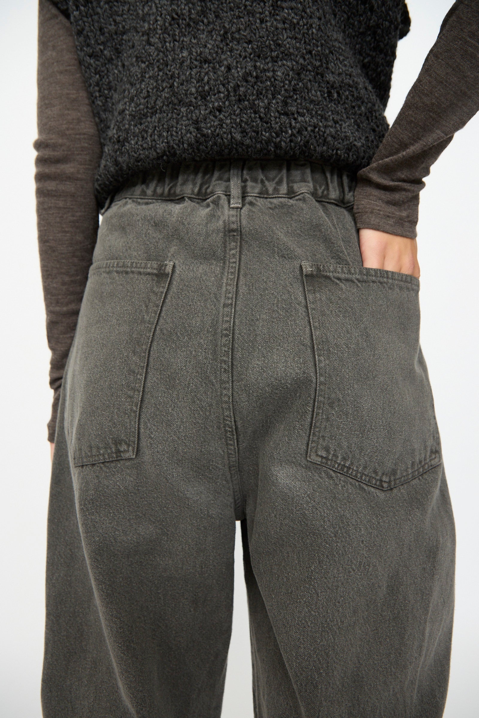 Someone is wearing SONO’s Cotton Jah Jeans in Off Black—high-waisted, loose-fit organic denim with back pockets—paired with a textured black top, right hand resting on their hip.