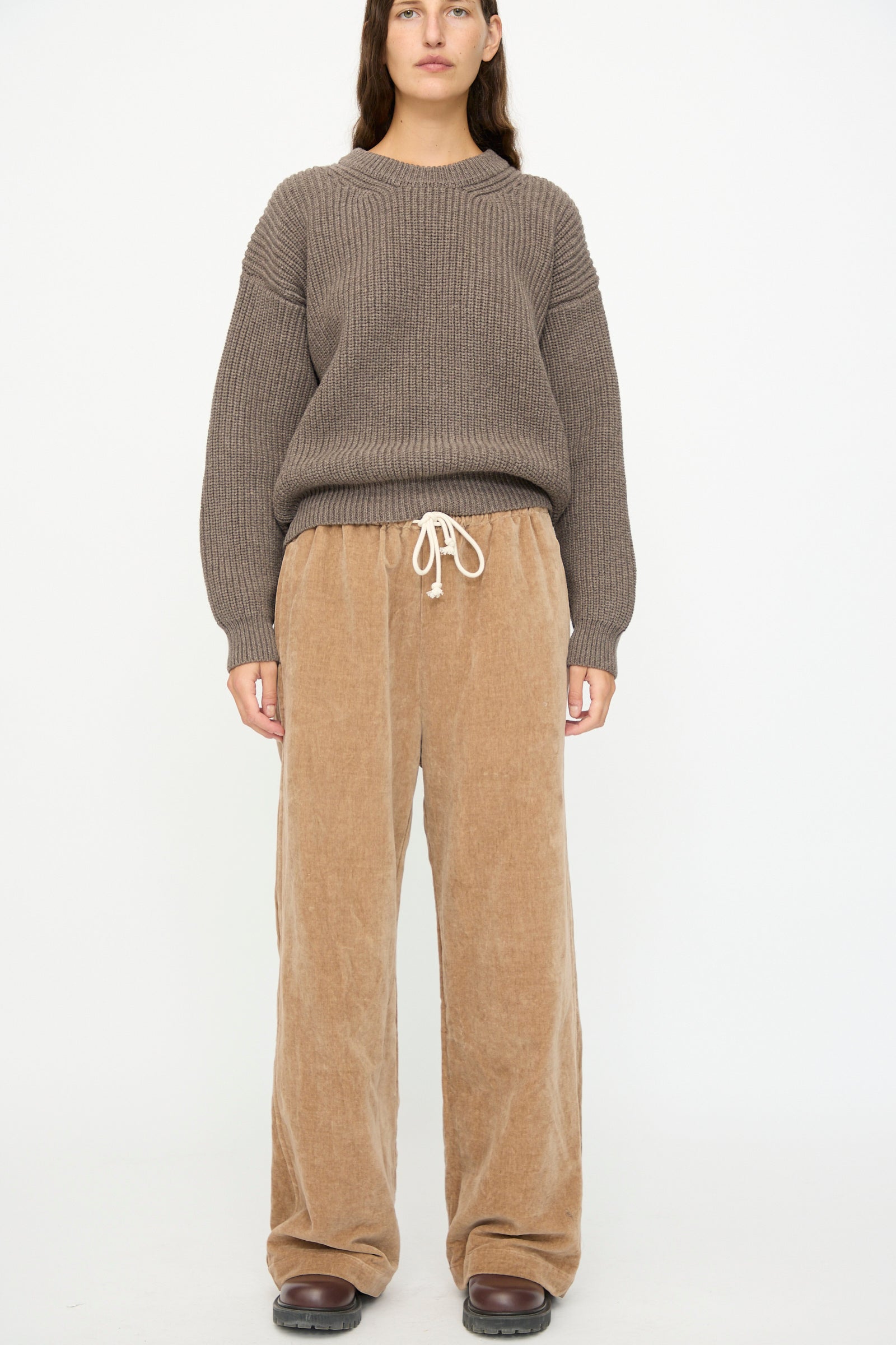 A person wears the SONO Johnny Jogger in Desert Rose with a brown ribbed sweater and brown shoes, standing against a plain white background.
