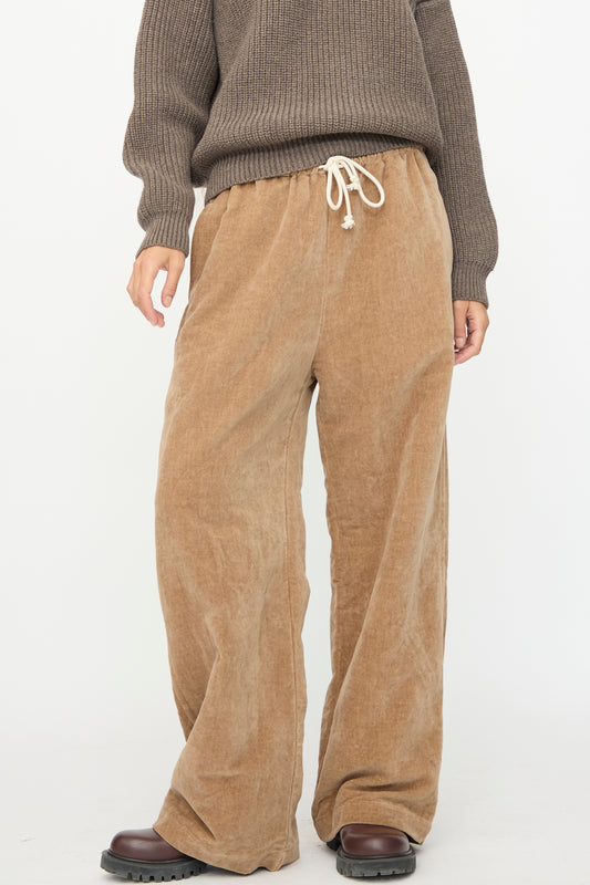A person wears the SONO Johnny Jogger in Desert Rose with a brown ribbed sweater and black platform shoes, standing against a plain white background.