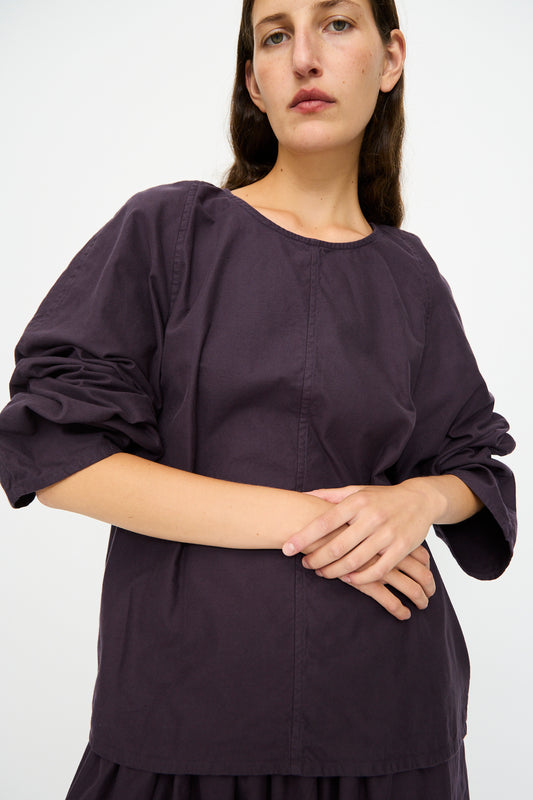 A person wears the SONO Tiga Top in Dark Grape, a loose-fitting, long-sleeved oversized shirt, standing against a plain light background with hands crossed at the waist.