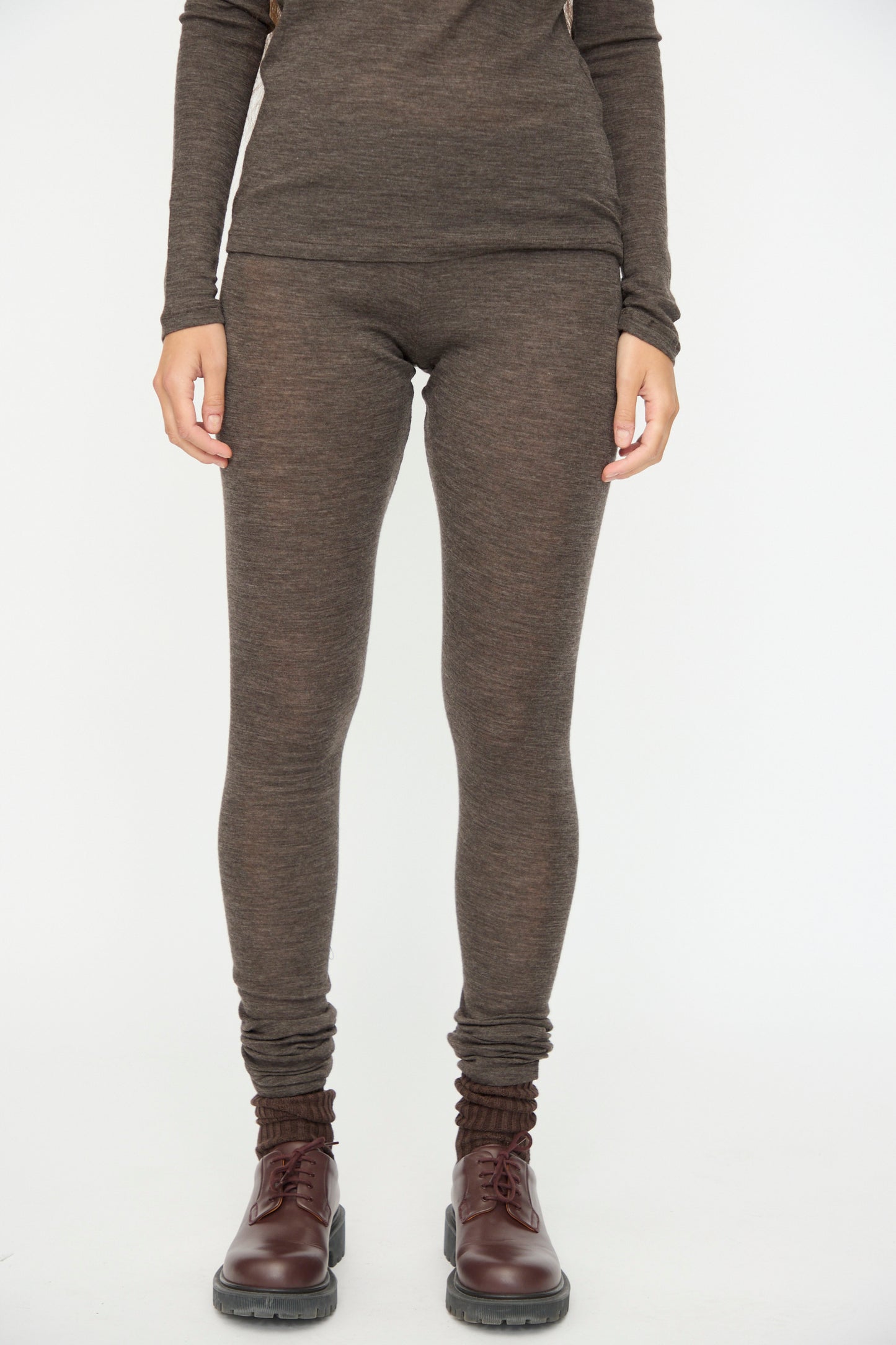 A person wearing SONO's Wool Lupo Leggings in Charcoal and a long-sleeve brown top with dark brown lace-up boots, standing against a plain white background.