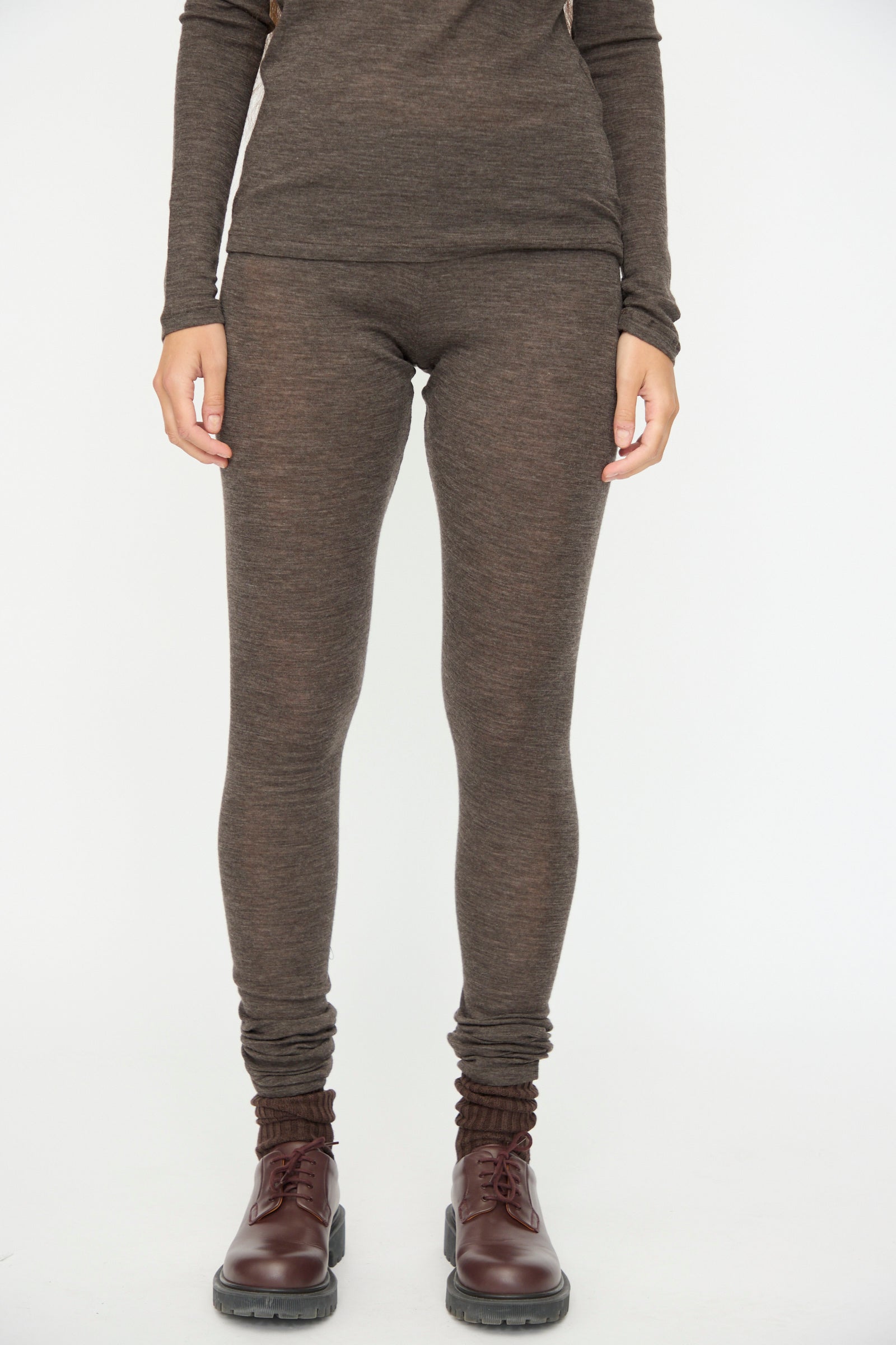 A person wearing SONO's Wool Lupo Leggings in Charcoal and a long-sleeve brown top with dark brown lace-up boots, standing against a plain white background.