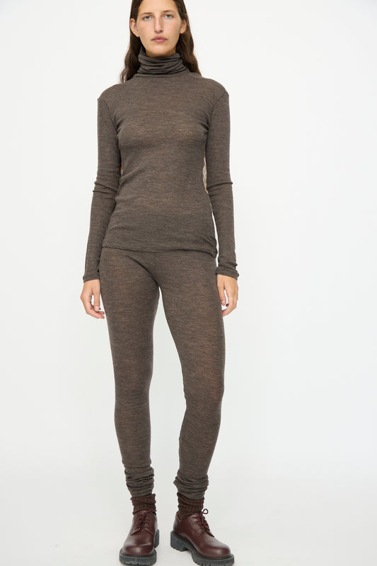 A person models SONO's Wool Lupo Leggings in Charcoal with a brown merino wool turtleneck and lace-up boots, standing against a plain white background.