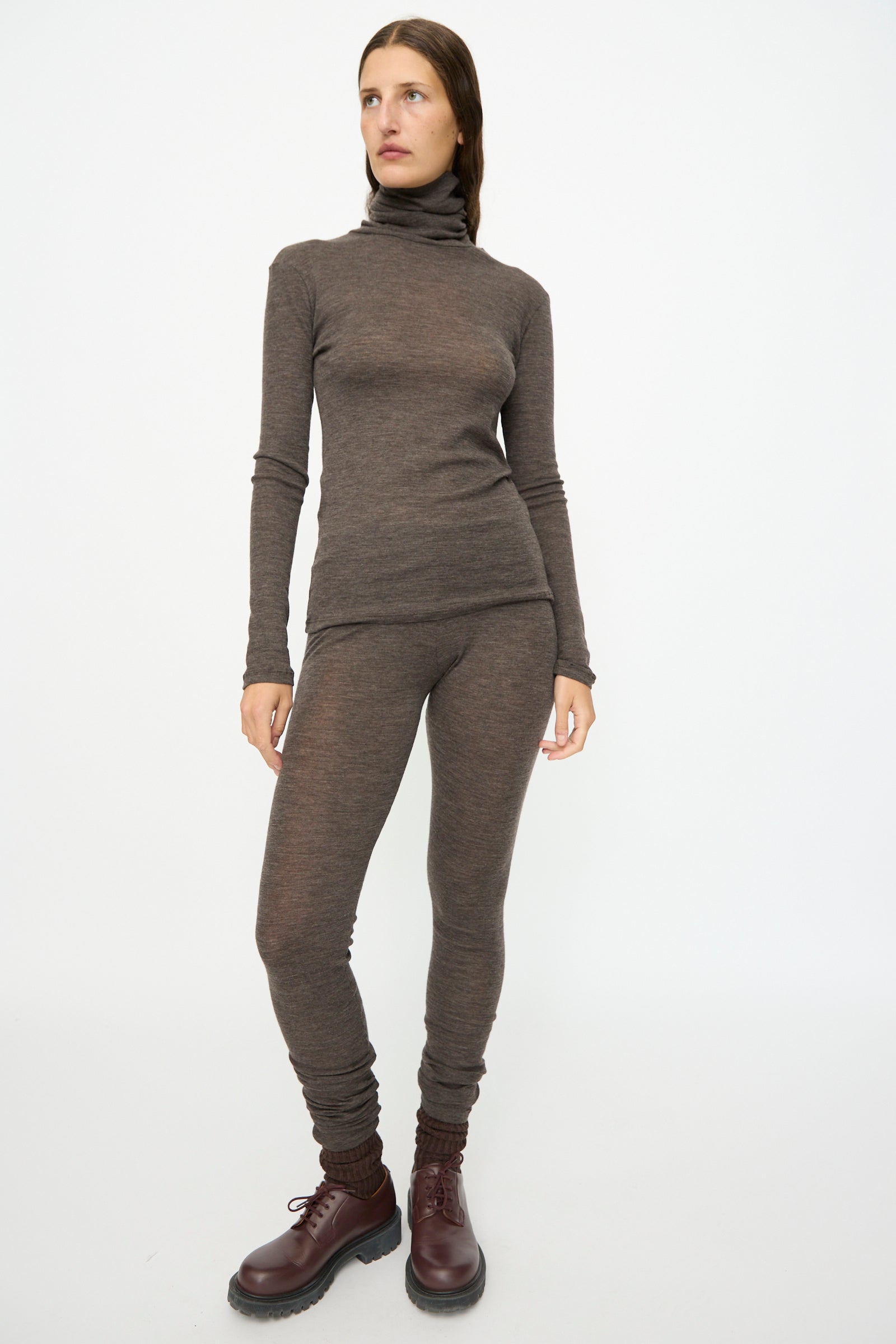 A person wearing the SONO Wool Roberta Rollneck in Charcoal and leggings with maroon lace-up boots, standing against a plain white background.