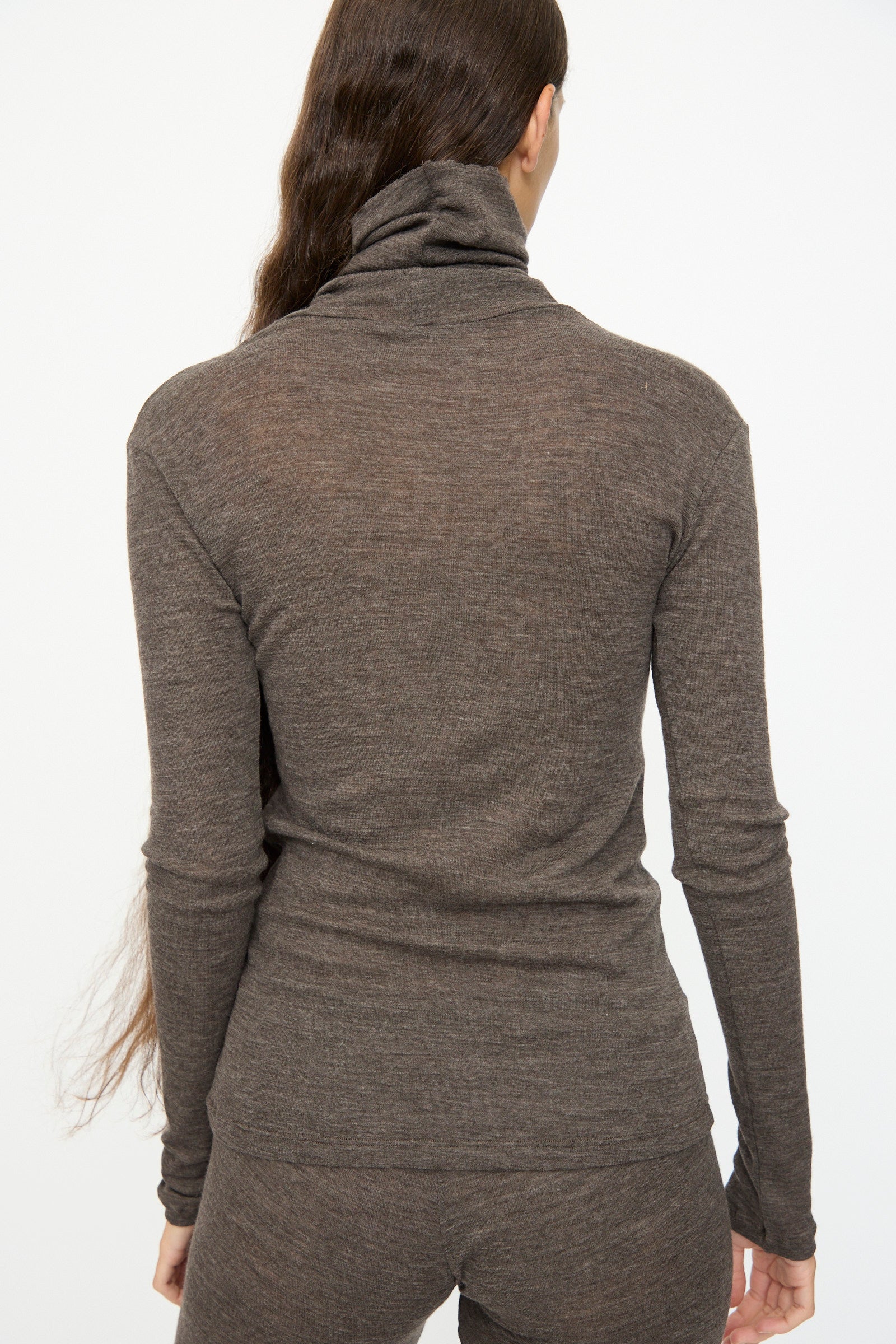 Person with long brown hair, seen from behind against a plain white background, wears the SONO Wool Roberta Rollneck in Charcoal with matching slim fit pants.