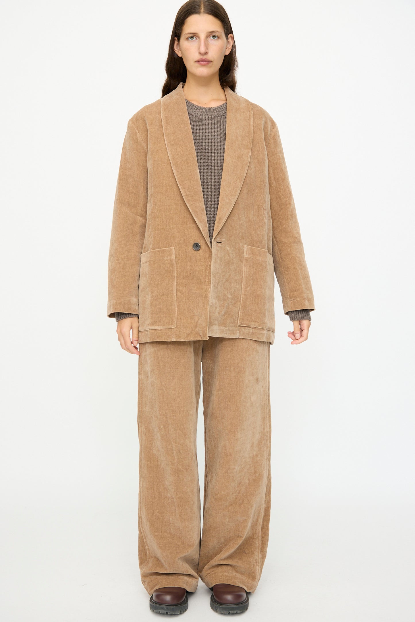 A person faces forward against a plain white background, wearing the SONO Yoyogi Jacket in Desert Rose styled as an oversized blazer with wide-legged pants and a brown top.