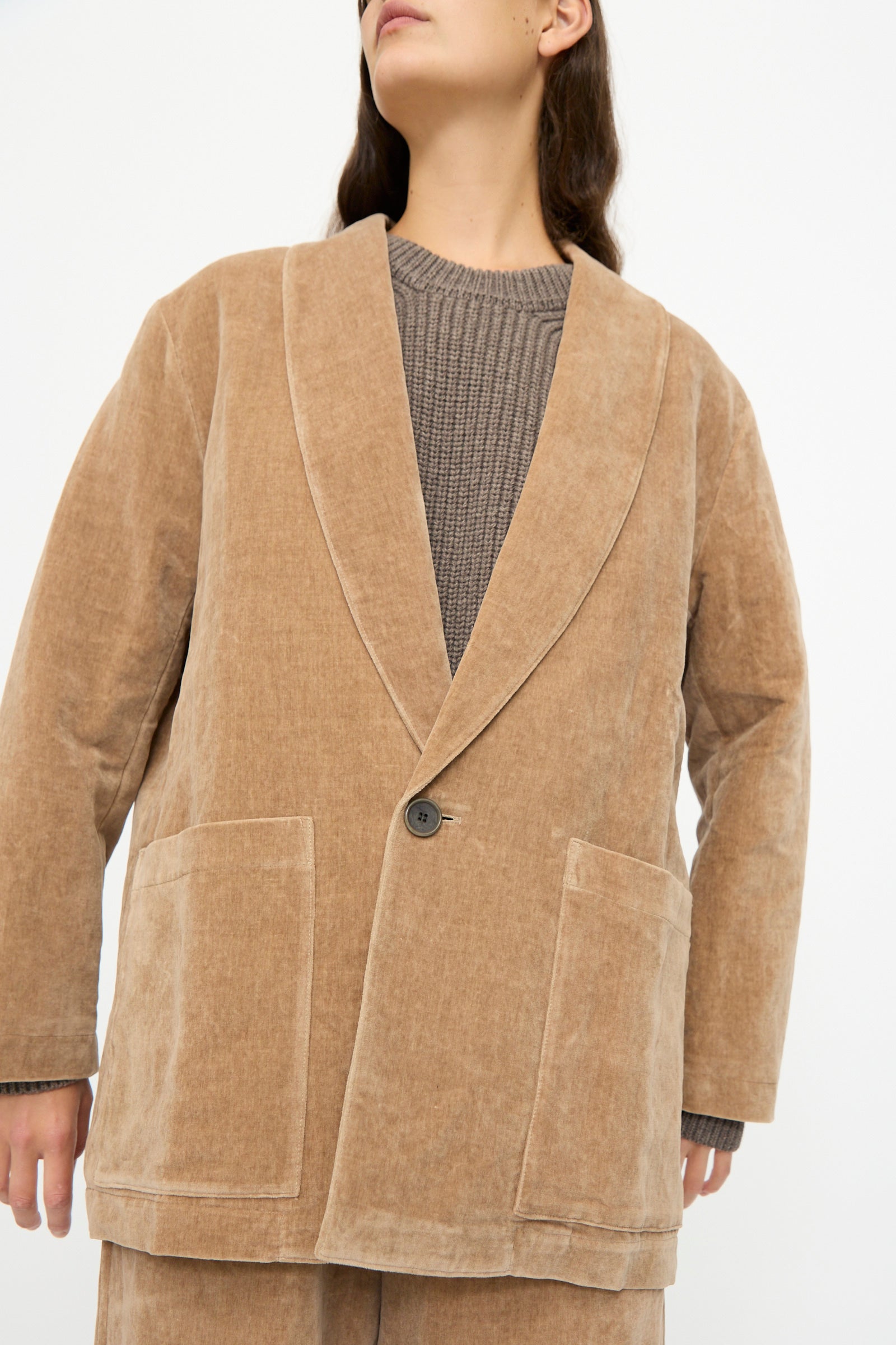 Someone wearing the SONO Yoyogi Jacket in Desert Rose—an oversized corduroy blazer with large front pockets and a single button—over a gray knit sweater, standing against a plain background.
