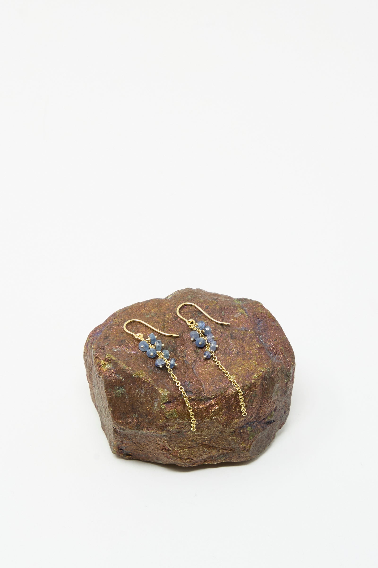 Stephanie Schneider Gold Plated Sterling Silver Earrings with Blue Sapphires, displayed on a brown stone against a plain white background.