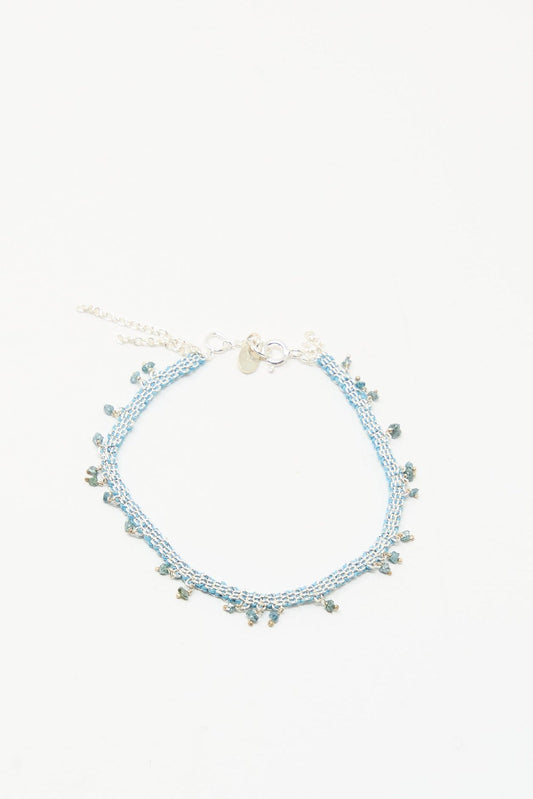 The Stephanie Schneider Silver and Silk Bracelet with Raw Blue Diamonds features delicate light blue silk, accented with raw blue diamonds and a silver clasp, displayed on a plain white background.