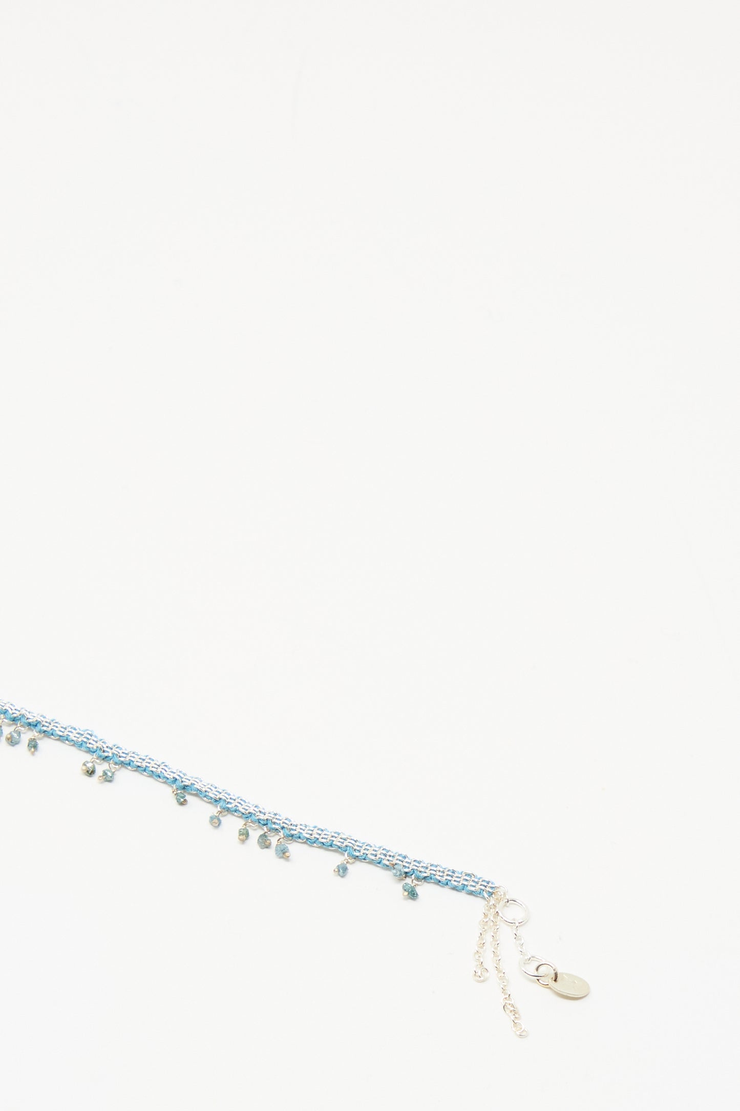 The Stephanie Schneider Silver and Silk Bracelet features raw blue diamonds and a silver clasp, displayed diagonally against a plain white background.