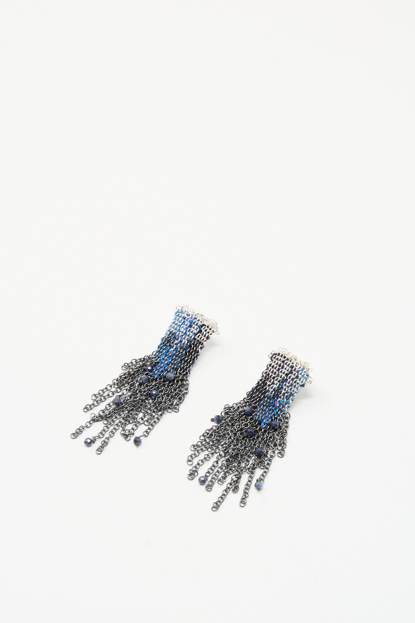 Stephanie Schneider’s Sterling Silver and Silk Earrings in Blue with Sapphires feature black and blue chain fringe cascading from a small white base, displayed on a plain white background.