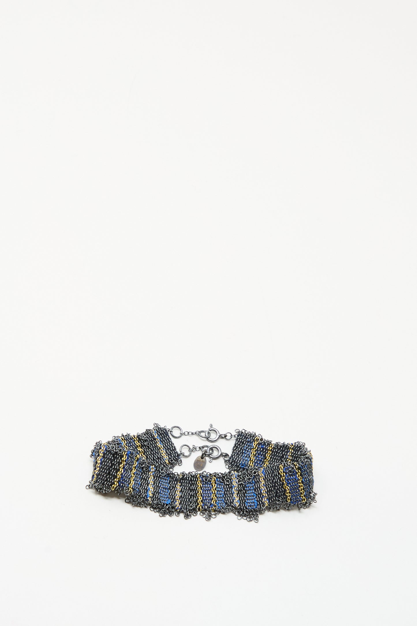 The Silver and Silk Woven Bracelet in Blue by Stephanie Schneider showcases a ruffled design with blue, gold, and dark metallic chains, finished with a lobster clasp, set against a plain white background.