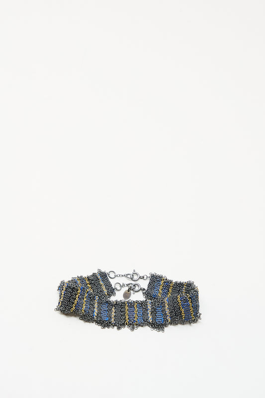 The Silver and Silk Woven Bracelet in Blue by Stephanie Schneider showcases a ruffled design with blue, gold, and dark metallic chains, finished with a lobster clasp, set against a plain white background.