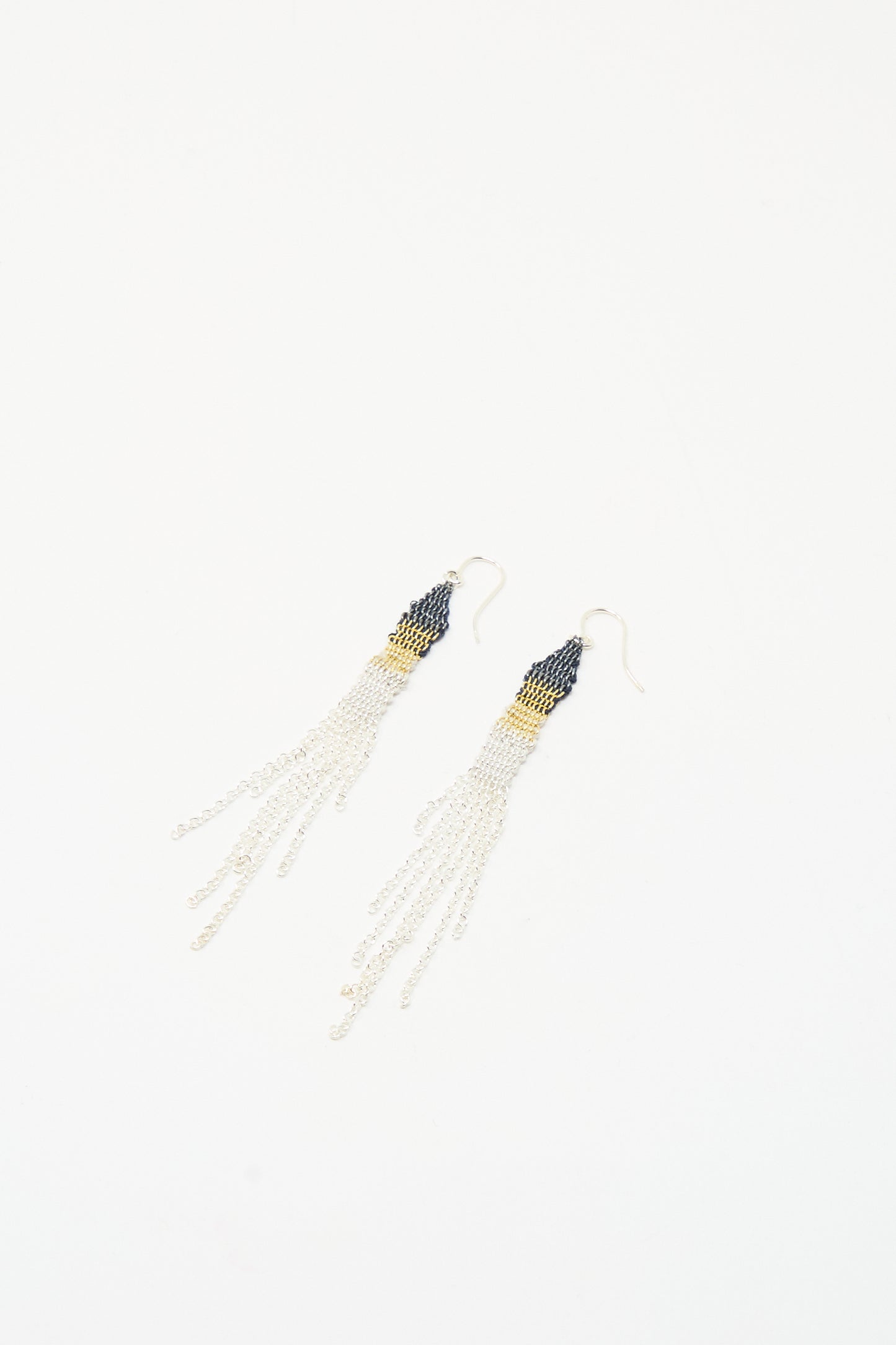 The Silver and Silk Woven Earrings by Stephanie Schneider feature dark beaded tops, gold accents, and long sterling silver chains, shown on a white background.