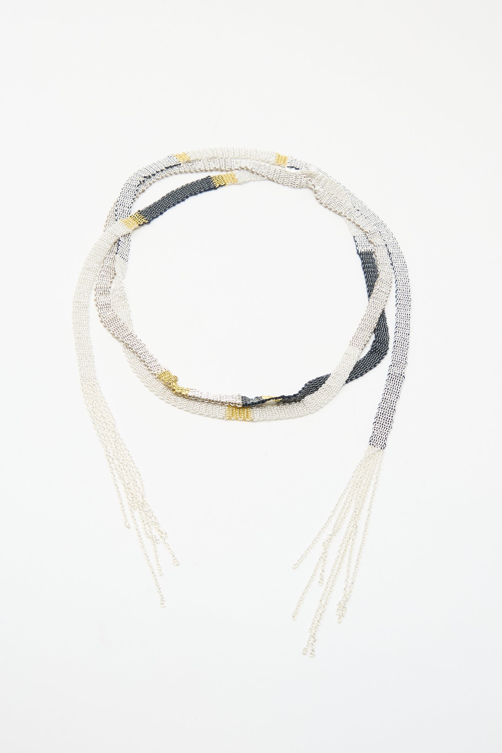 The Silver and Silk Woven Shawl Necklace by Stephanie Schneider features alternating white, gold, and black beads with loose strands on both ends, reminiscent of a sterling silver shawl, displayed on a white background.