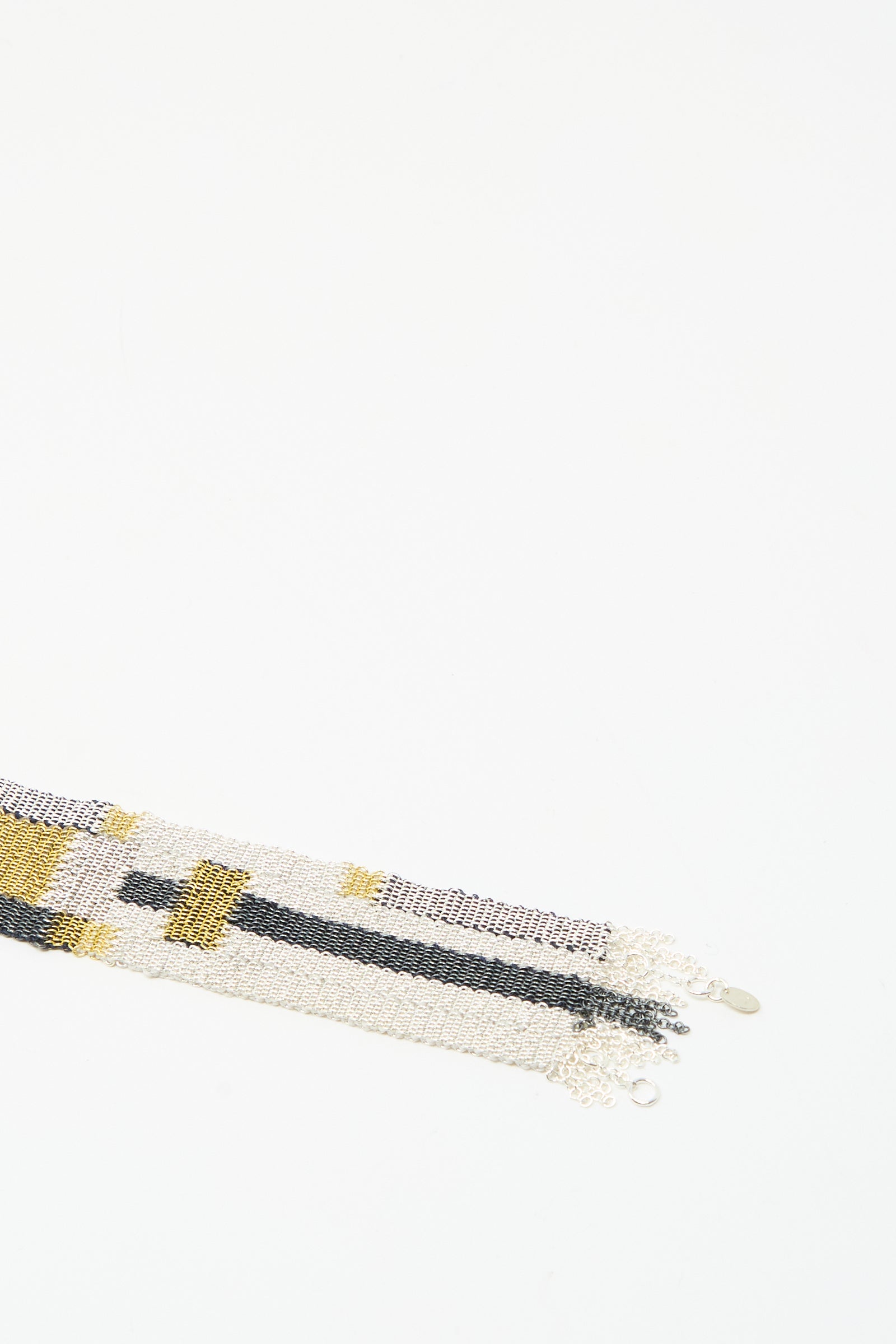 A close-up of the Stephanie Schneider Silver Oxidized, Gold Plated and Silk Woven Bracelet, featuring intricate patterns, displayed on a white background with empty space above.