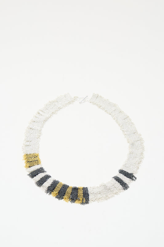 The Silver, Gold and Silk Woven Necklace by Stephanie Schneider features alternating white, black, and gold beads and a gold plated silver clasp, displayed against a plain white background.
