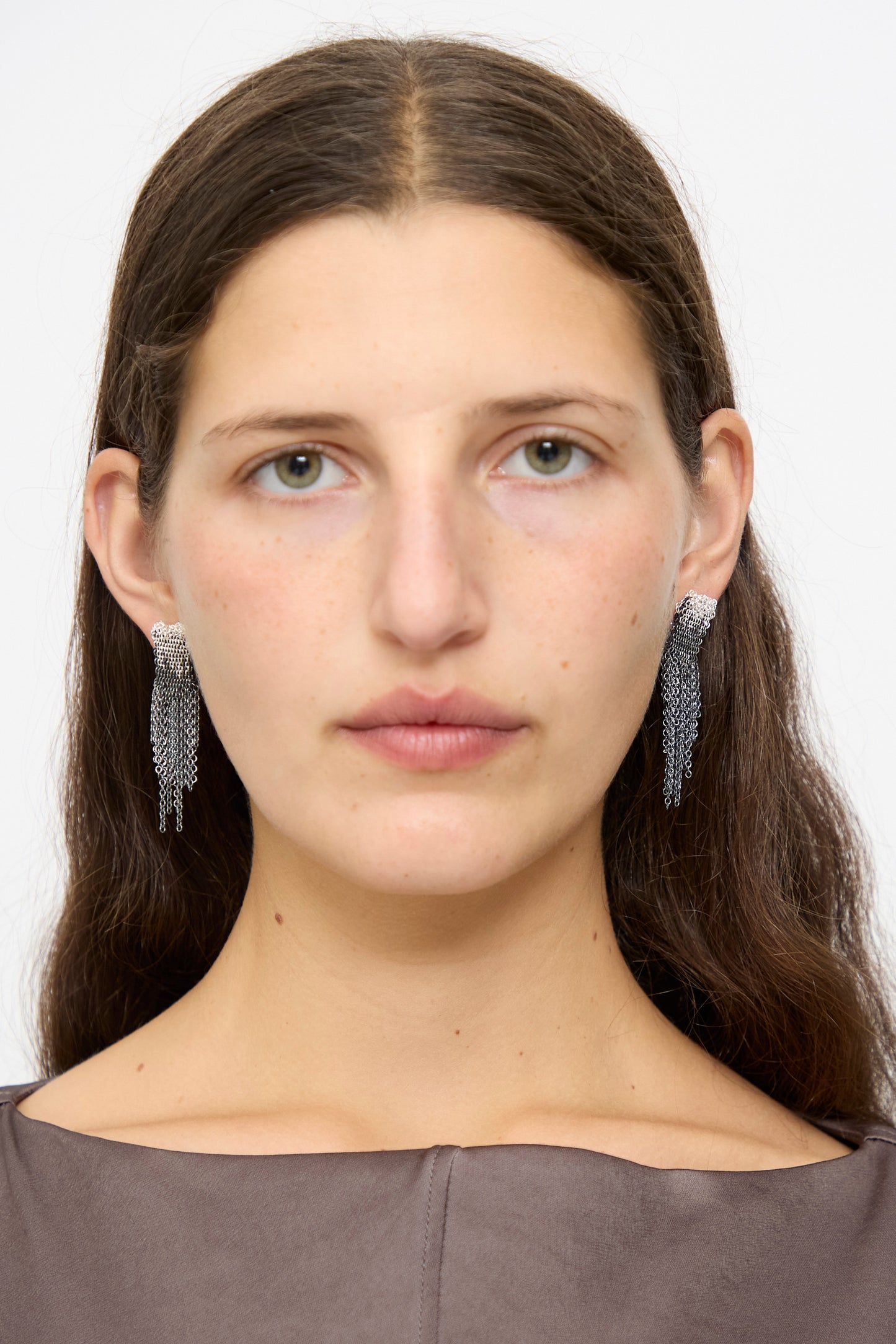 A woman with long brown hair wears Stephanie Schneider Sterling Silver Oxidized and Silk Earrings in Anthracite and a taupe top, facing forward against a plain white background.
