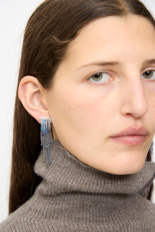 A woman with straight brown hair wears a taupe turtleneck and Stephanie Schneider Sterling Silver and Silk Earrings in Blue with Sapphires, looking toward the camera.