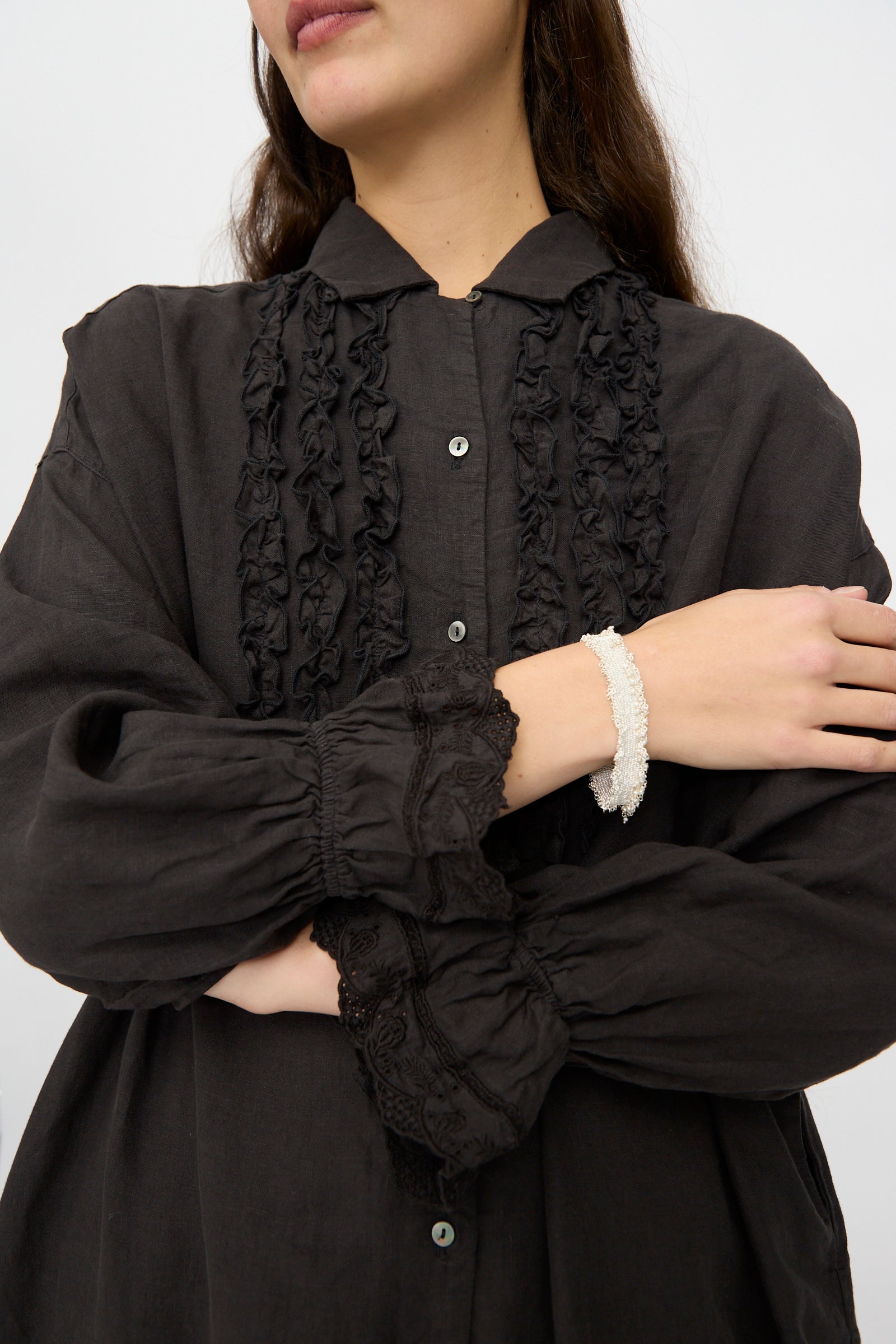 A woman crosses her arms, highlighting the Stephanie Schneider Silver and Silk Woven Bracelet with Pearls on her wrist as she wears a black blouse with ruffled details and lace cuffs.