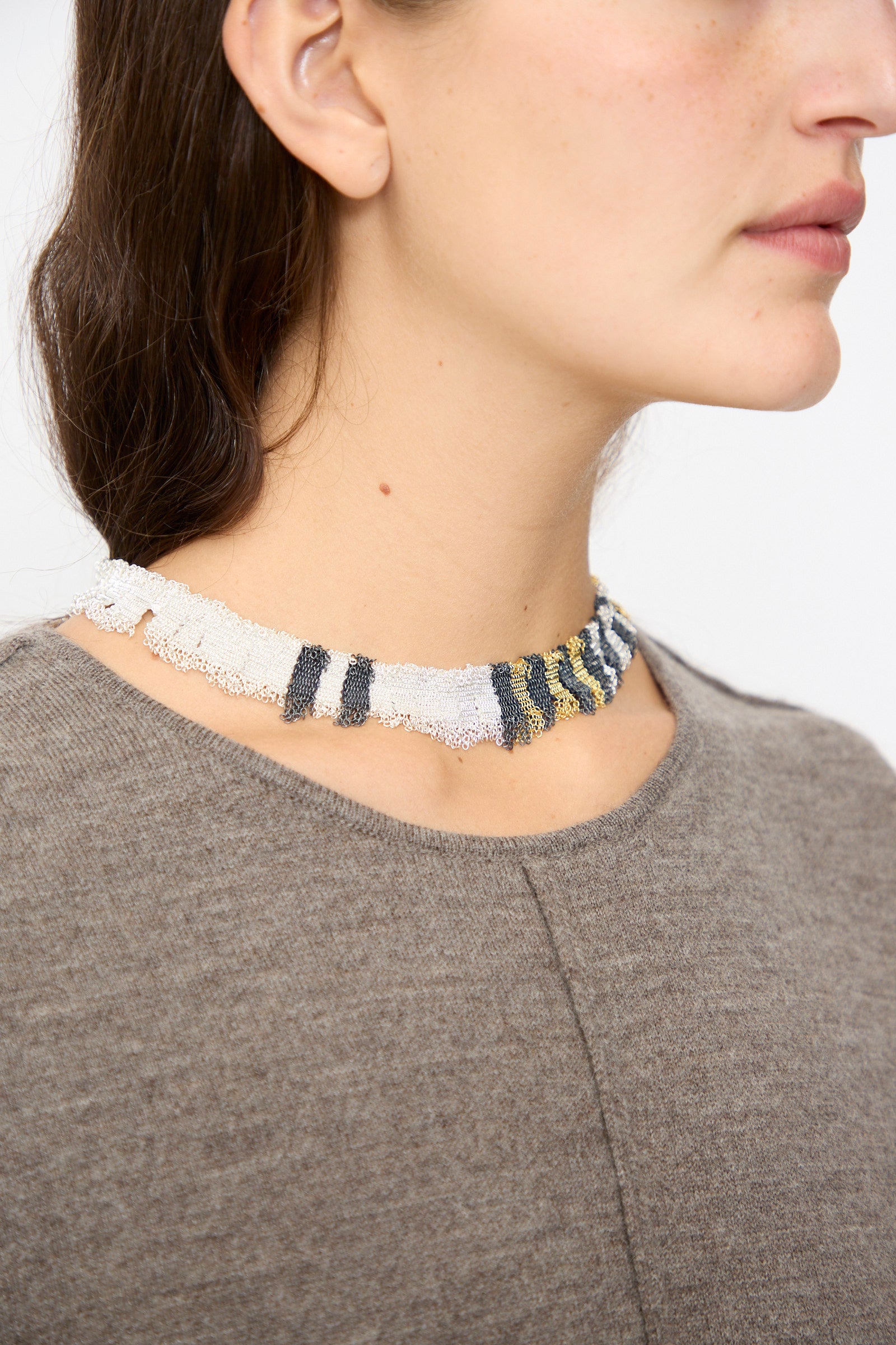 A person wears a textured knit gray top and a multicolored beaded choker, paired with the Stephanie Schneider Silver, Gold and Silk Woven Necklace.