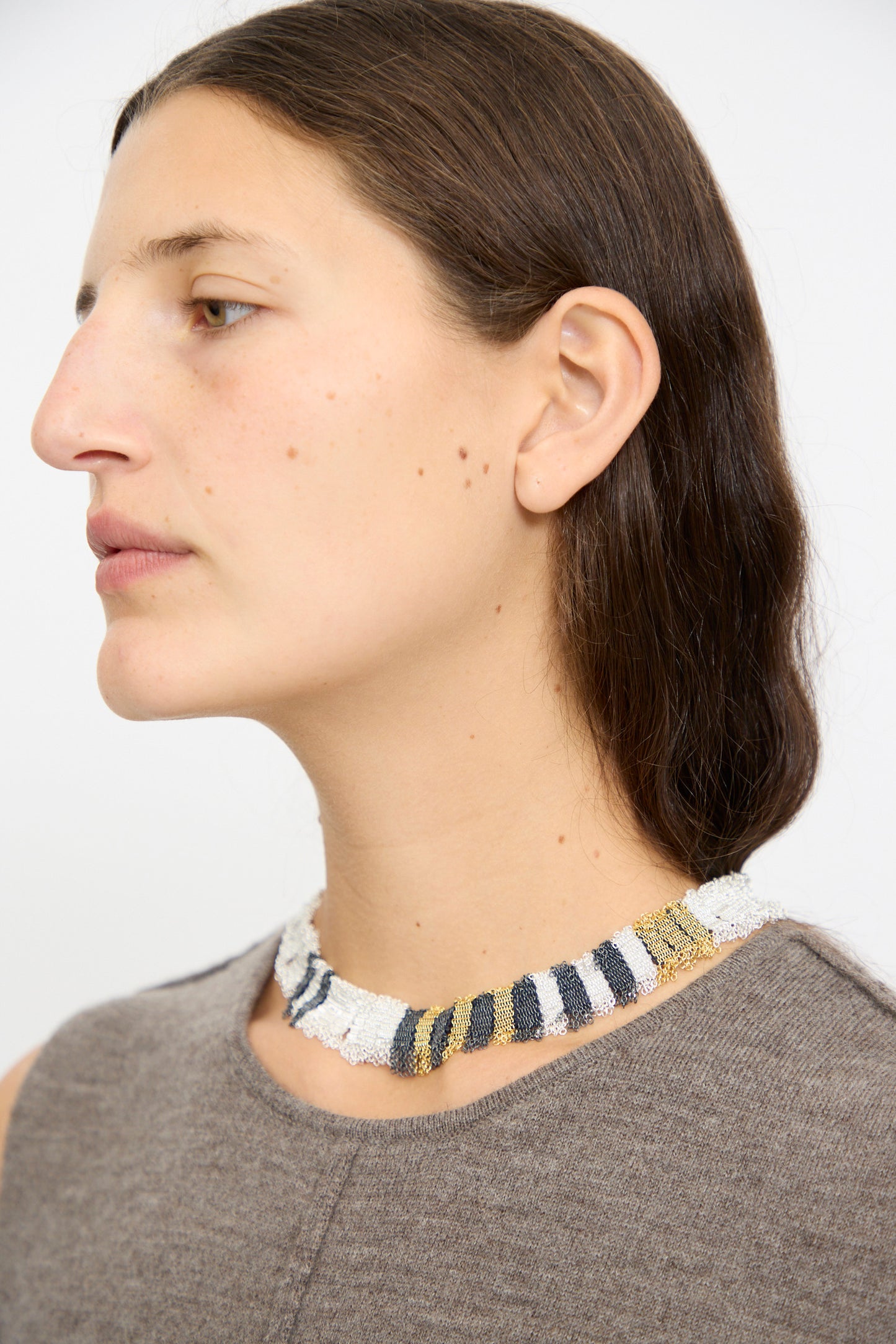 A woman with long brown hair wears a sleeveless gray top and the Stephanie Schneider Silver, Gold and Silk Woven Necklace.
