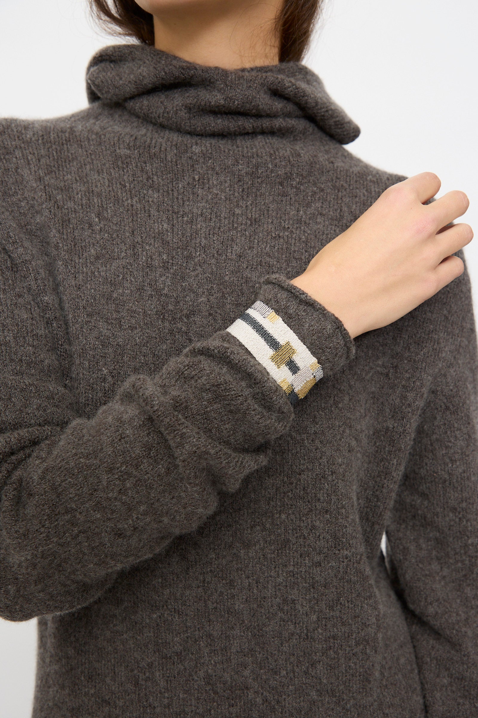 A person in a brown turtleneck with striped cuff detail raises their right hand, showcasing the Stephanie Schneider Silver Oxidized, Gold Plated and Silk Woven Bracelet.