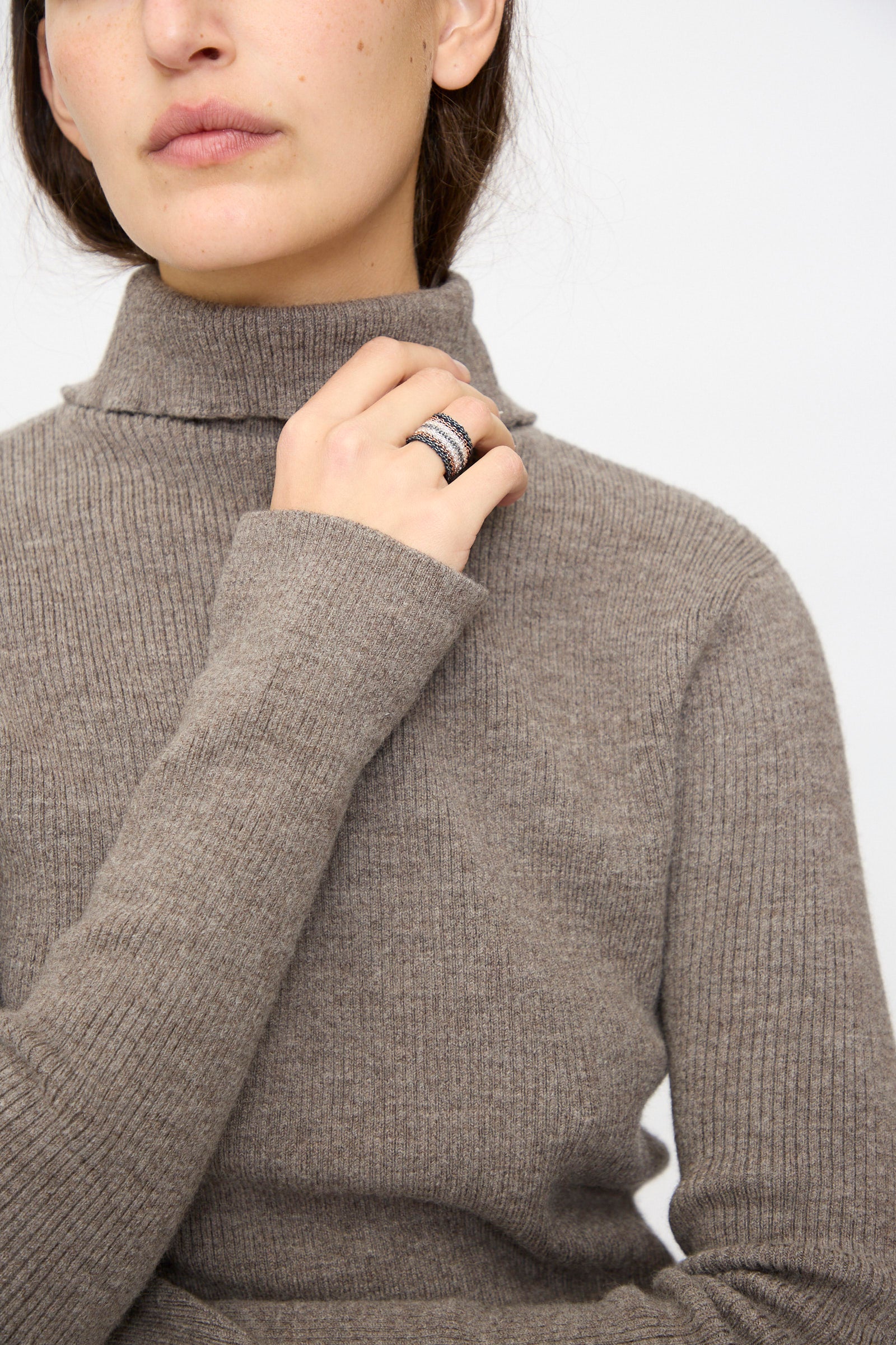 A person in a taupe ribbed turtleneck poses with their hand near their chin, showcasing the Stephanie Schneider Silver, Rose Gold Plated and Silk Woven Ring.