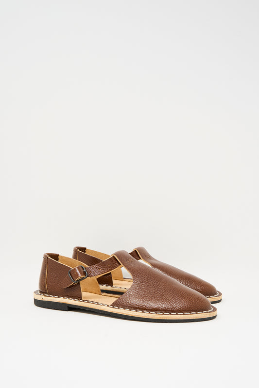 The Steve Mono Artisanal Sandal 10/12 in Brandy features vegetable-tanned leather, buckle straps, and flat recycled rubber soles, showcased on a plain white background.