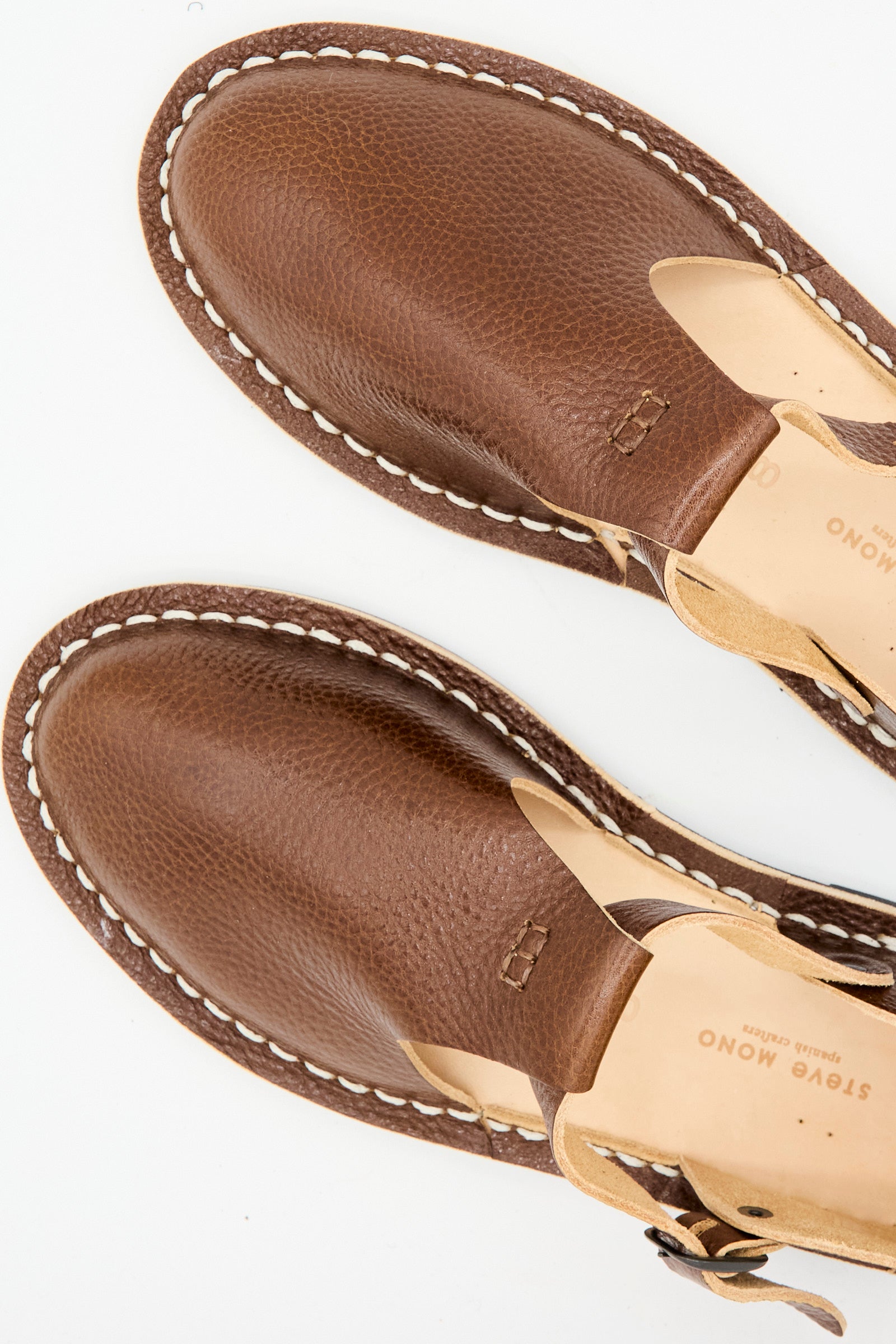 Close-up of the Steve Mono Artisanal Sandal 10/12 in Brandy, made from vegetable-tanned leather with visible stitching, buckle detail, and a recycled rubber sole, shown on a white background.