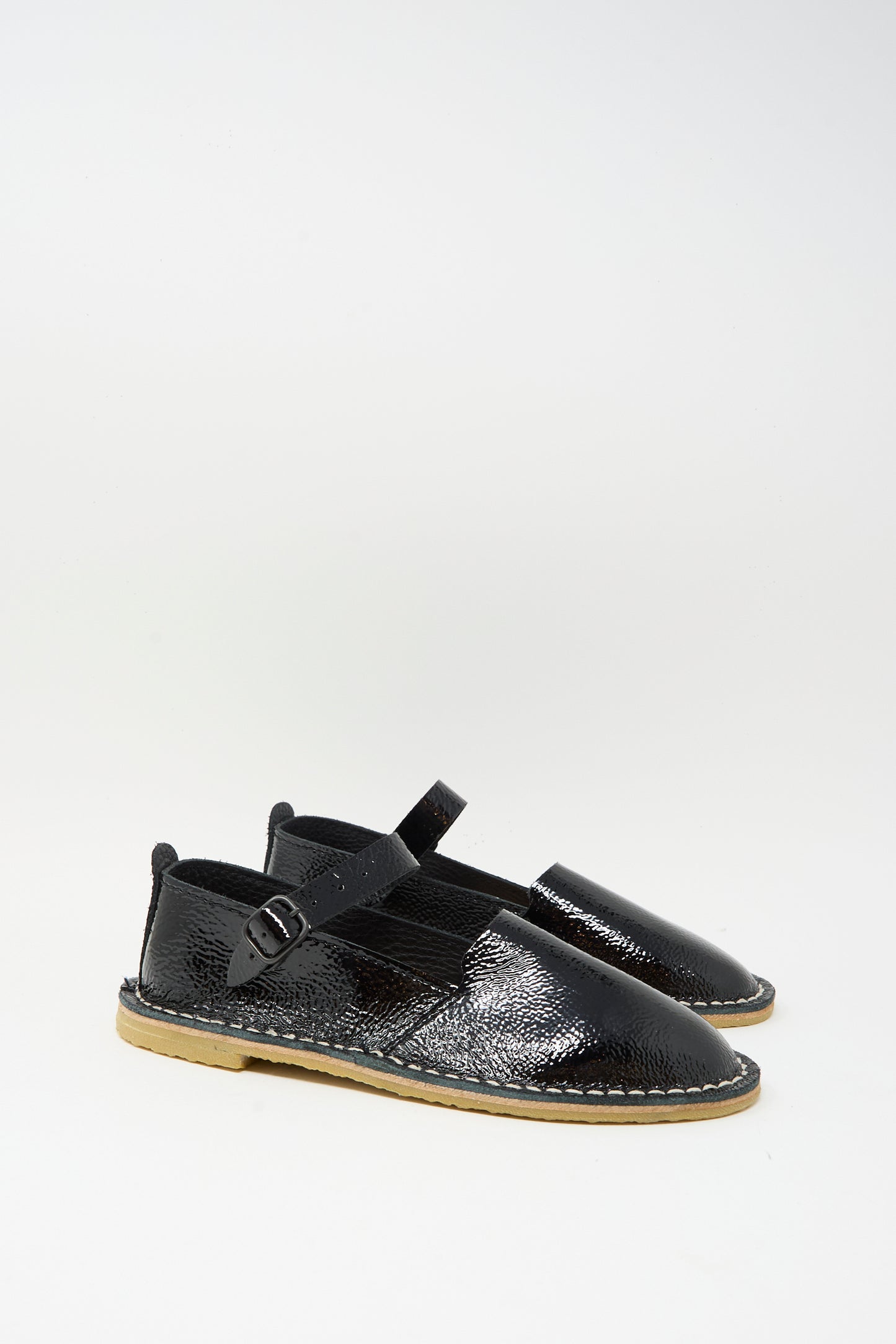 The Steve Mono Mary Jane in Glossy Black features buckled straps and light brown recycled rubber soles, shown against a plain white background.