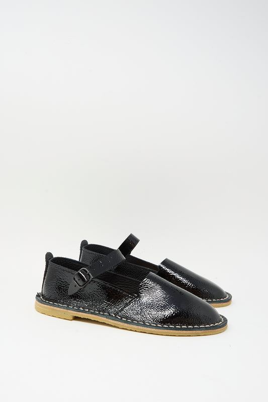 The Steve Mono Mary Jane in Glossy Black features buckled straps and light brown recycled rubber soles, shown against a plain white background.