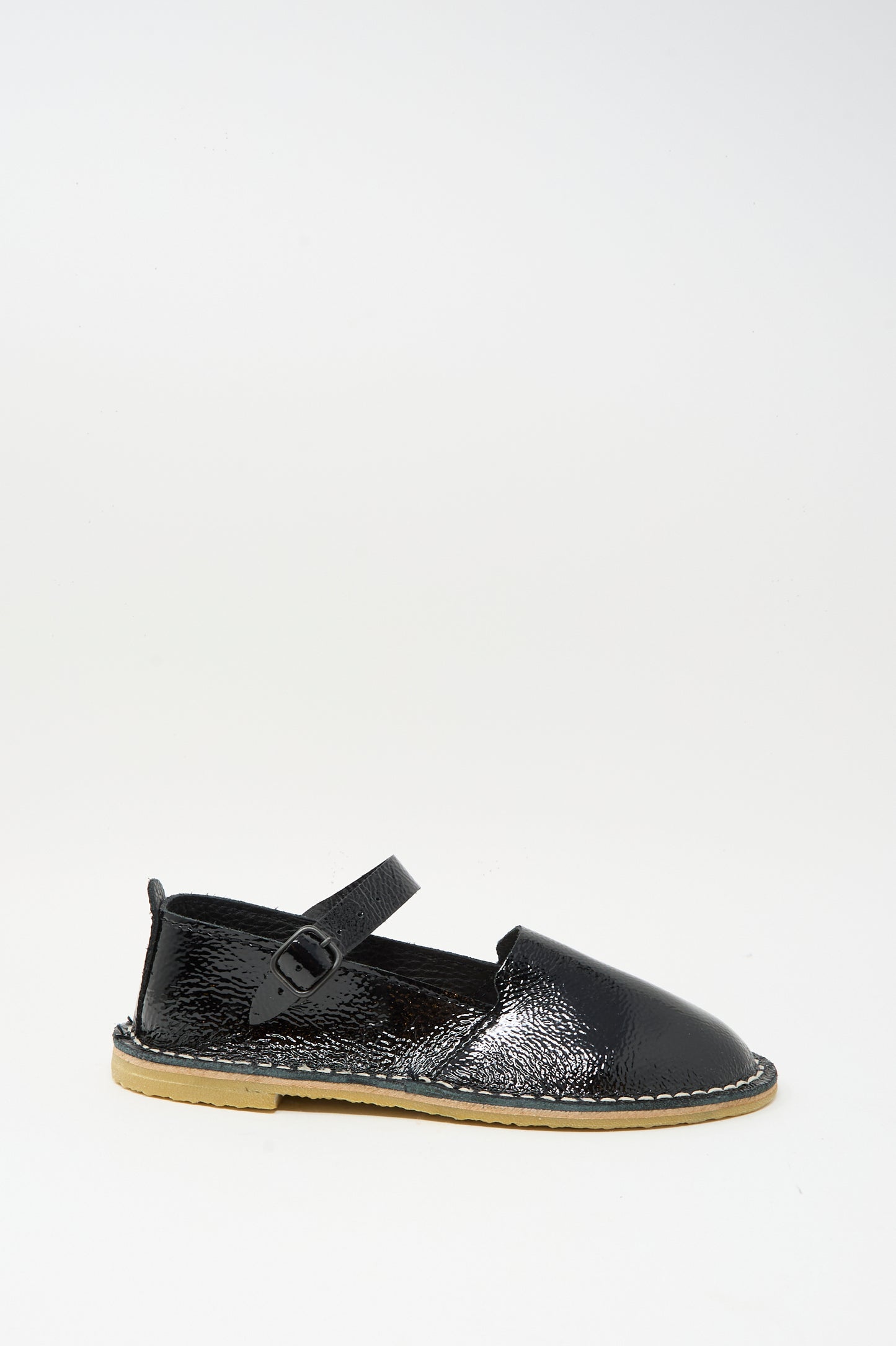 The Steve Mono Mary Jane in Glossy Black features a single black patent leather sandal with an ankle strap and buckle, light tan sole, and visible stitching, all shown against a plain white background.