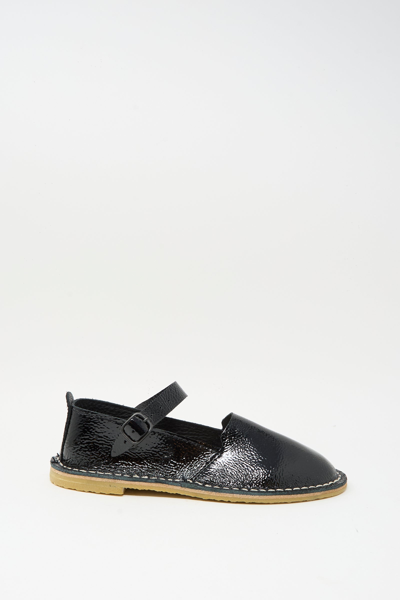 The Steve Mono Mary Jane in Glossy Black features a single black patent leather sandal with an ankle strap and buckle, light tan sole, and visible stitching, all shown against a plain white background.